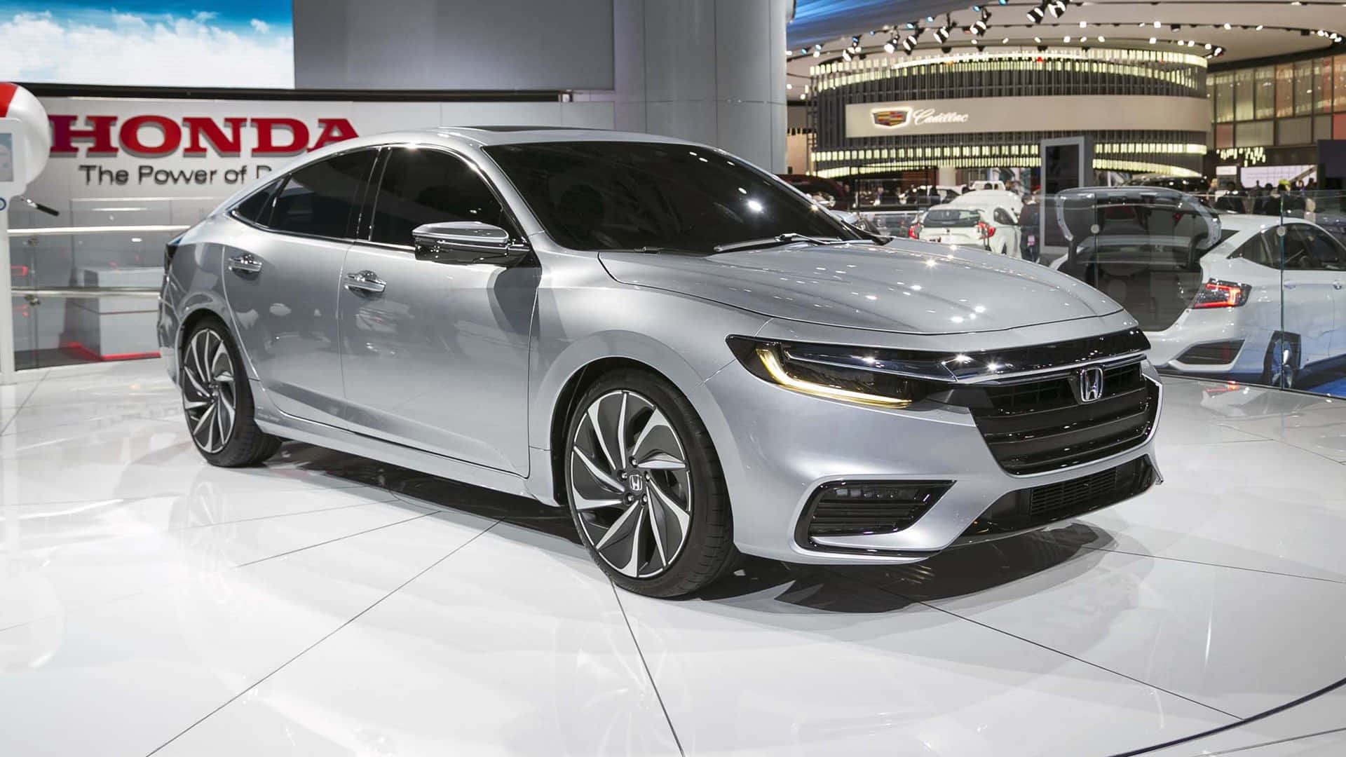Honda Insight 桌布 壁紙 — 一輛時尚的銀色本田轎車在明亮的展廳燈光下閃閃發光，停放在拋光白色地板上，背景有品牌標誌。