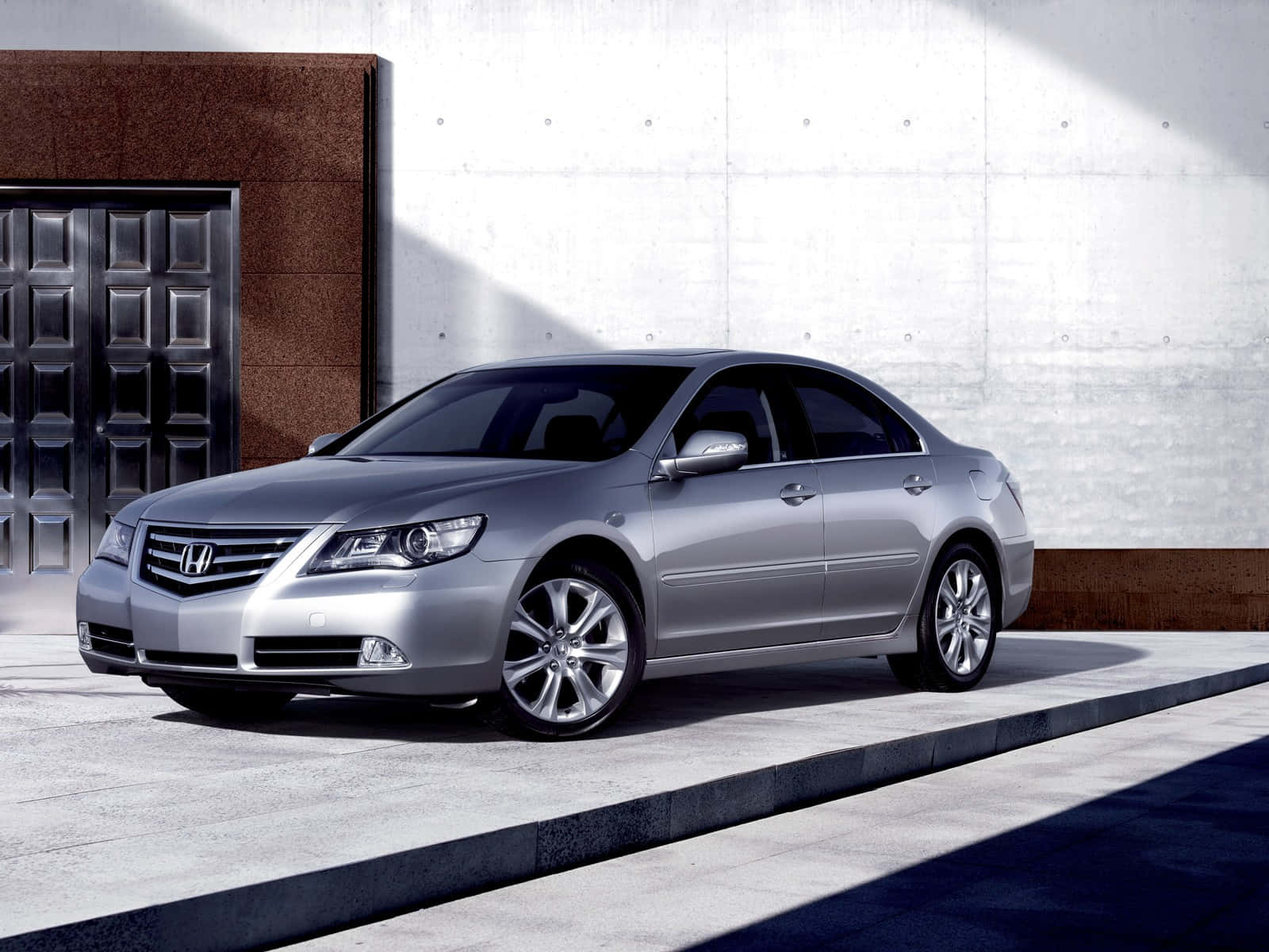 Honda Legend 桌布 壁紙 — 一輛時尚的銀色本田雅閣轎車停放在現代建築旁的混凝土行人道上，建築有深色門和紋理牆壁。