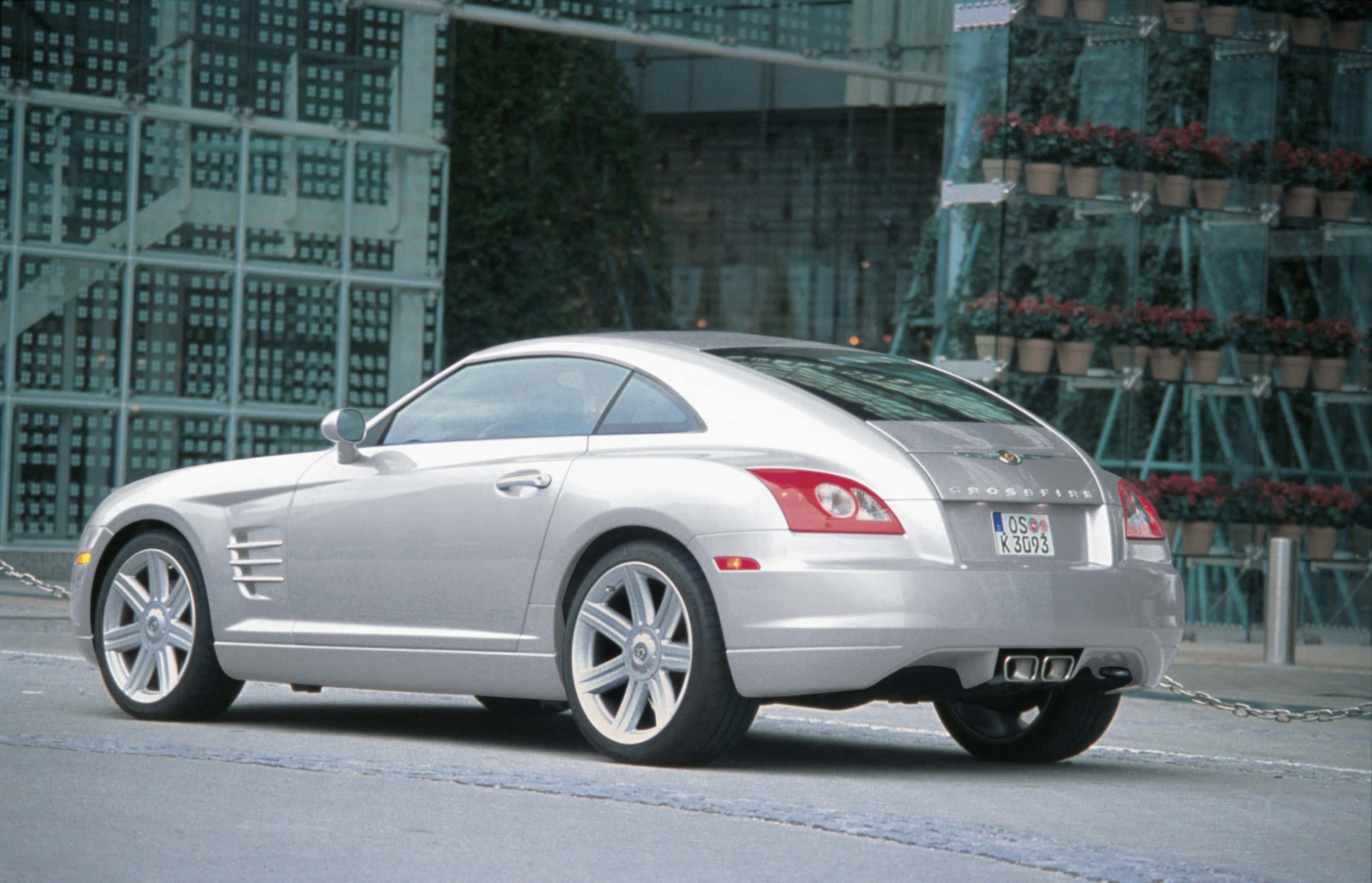 Chrysler Crossfire 桌布 壁紙 — 一輛時尚的銀色梅賽德斯-奔馳 SLR 邁凱倫跑車停放在城市街道上，背景是玻璃建築和盆栽植物。