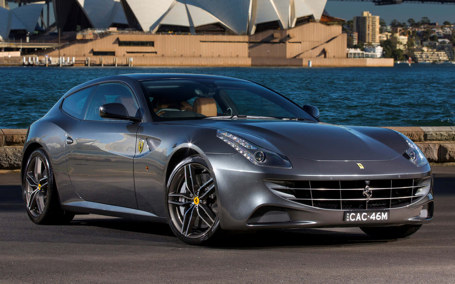 Ferrari Ff 桌布 壁紙 — 一輛時尚的銀色法拉利FF停在水邊，背景是悉尼歌劇院，在明亮的日光下。