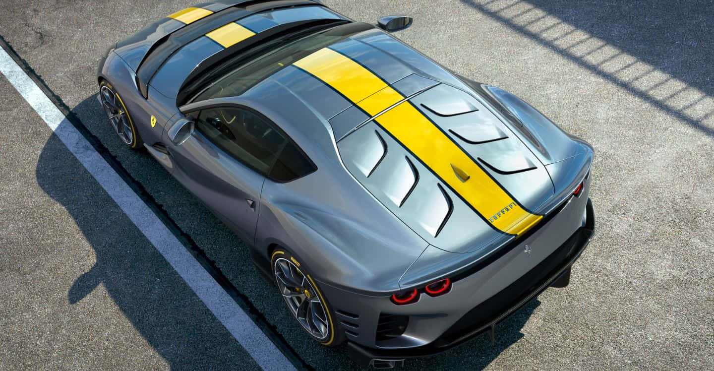 Ferrari 812 Superfast 桌布 壁紙 — 一輛時尚的銀色法拉利跑車，帶有醒目的黃色賽車條紋，停在陽光明媚的瀝青賽道上。