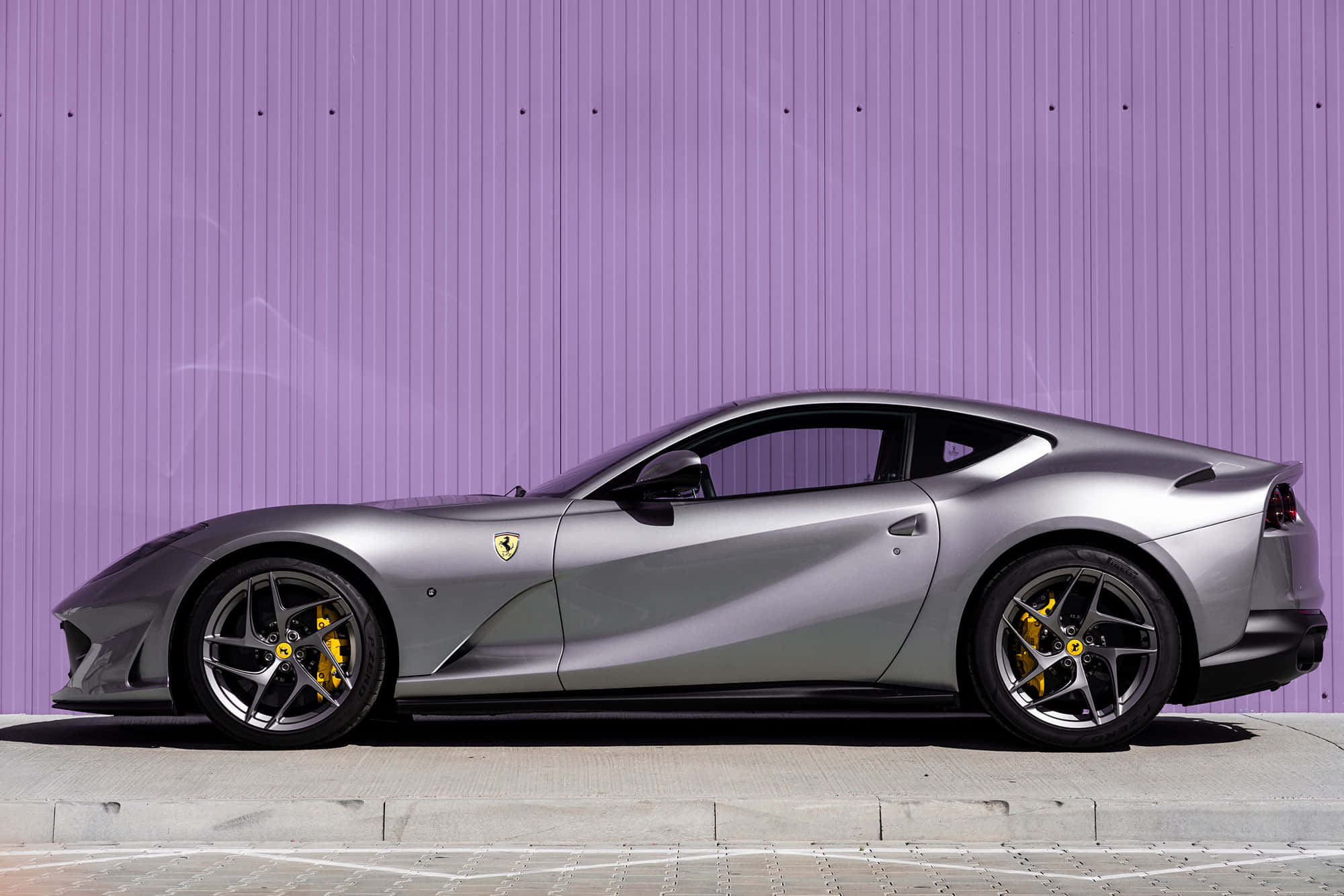 Ferrari 812 Superfast 桌布 壁紙 — 一輛時尚的銀色法拉利跑車，帶有黃色制動卡鉗，停在充滿活力的紫色波紋牆前。
