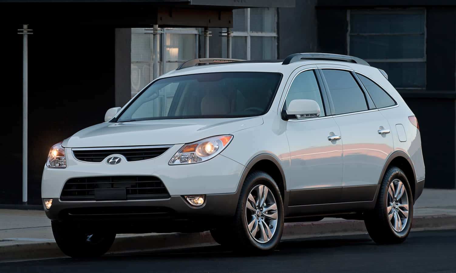 Hyundai Veracruz 桌布 壁紙 — 一輛時尚的銀色現代 Tucson SUV 在黃昏時停泊在城市的街道上，車頭燈亮起，背景是城市建築。
