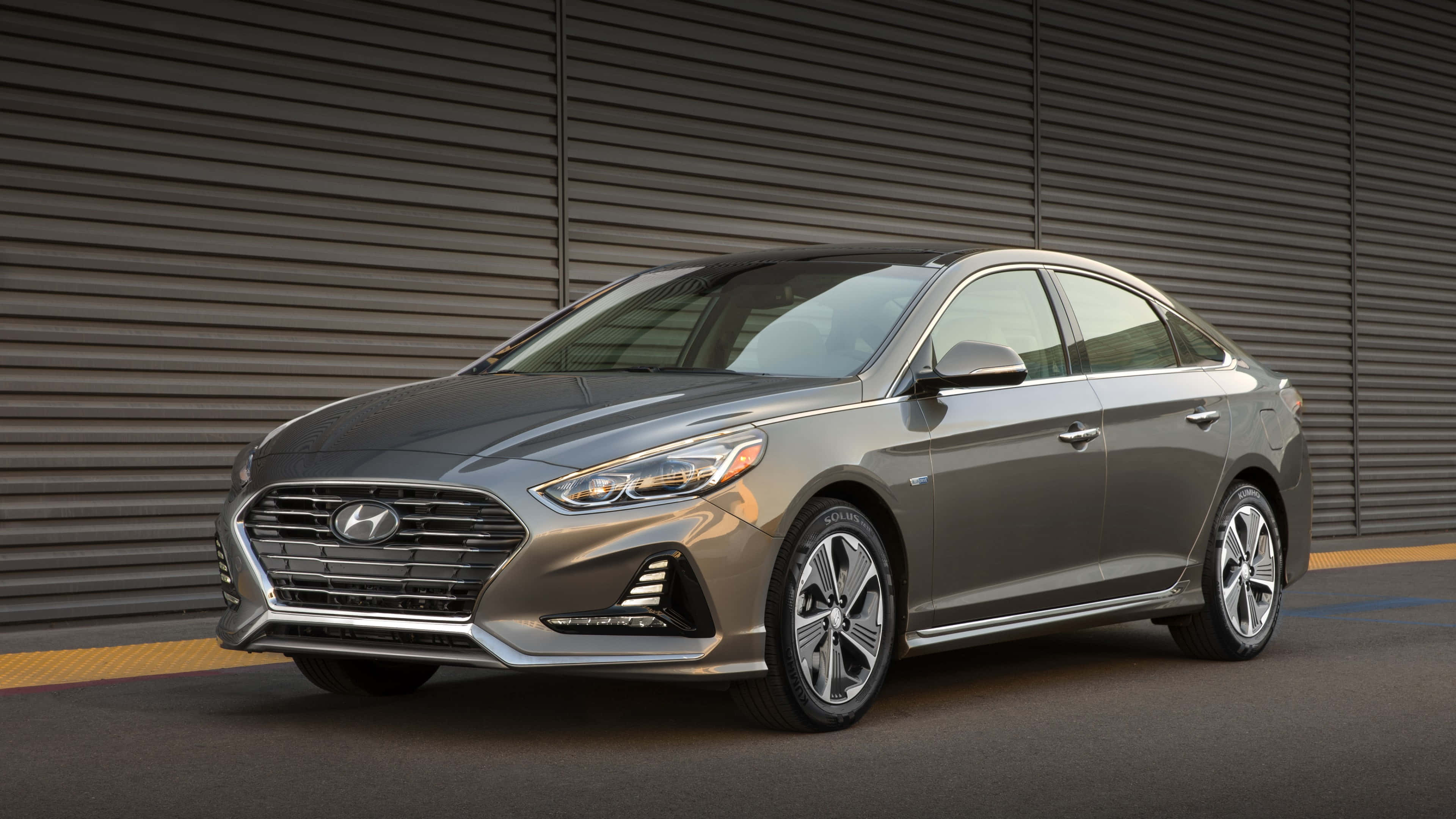 Hyundai Accent 桌布 壁紙 — 一輛時尚的銀色現代索納塔轎車停在深灰色波紋金屬牆前，帶有黃色路緣。