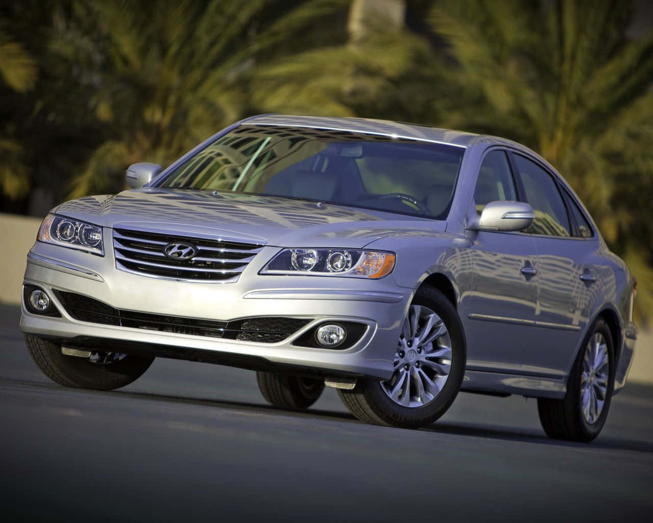 Hyundai Azera 桌布 壁紙 — 一輛時尚的銀色現代轎車在明亮的日光下，在棕櫚樹搖曳的背景中平穩地行駛在道路上。