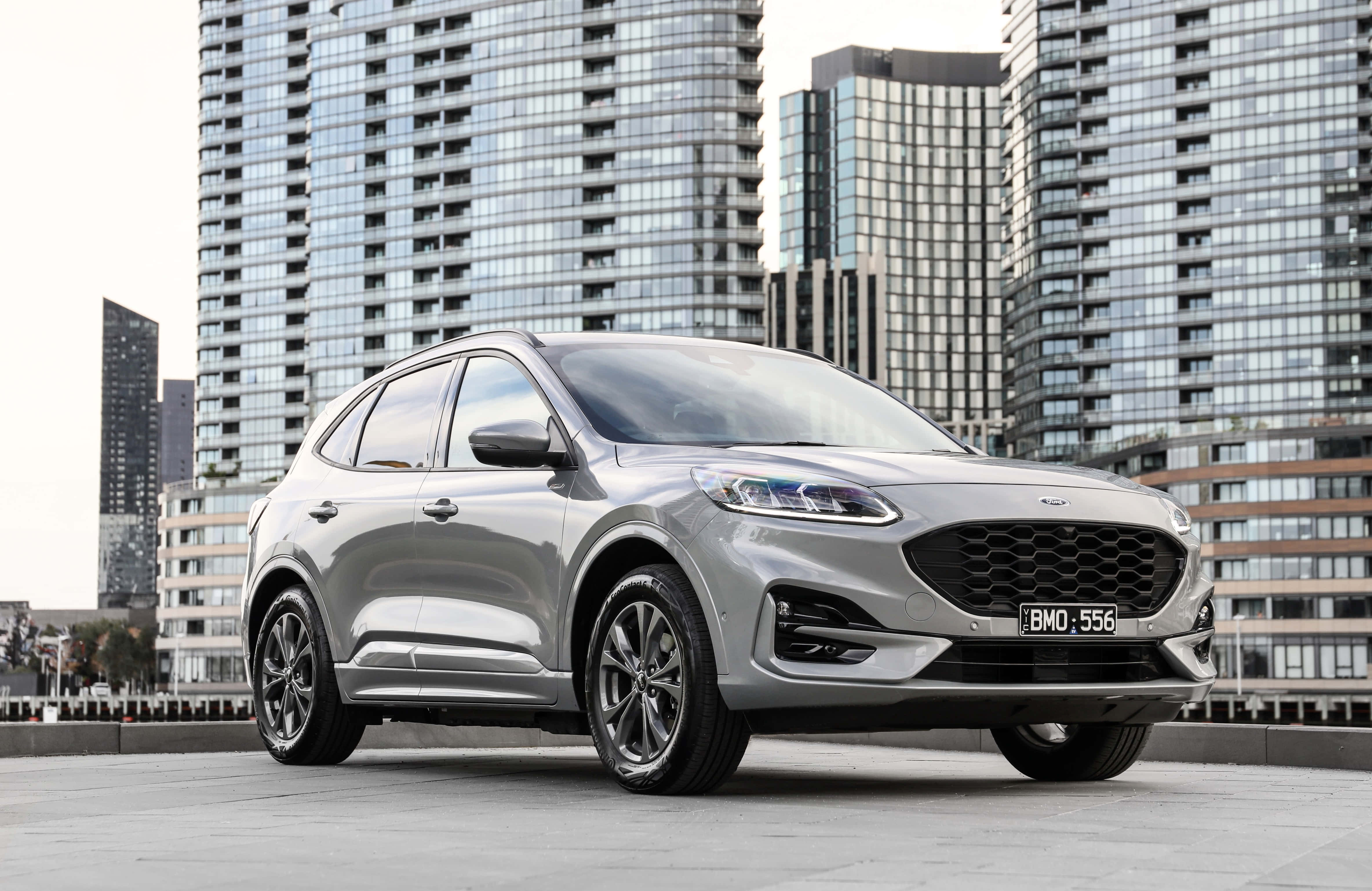 Ford Escape 桌布 壁紙 — 一輛時尚的銀色福特Kuga SUV停泊在屋頂上，背後有現代玻璃摩天大樓聳立。