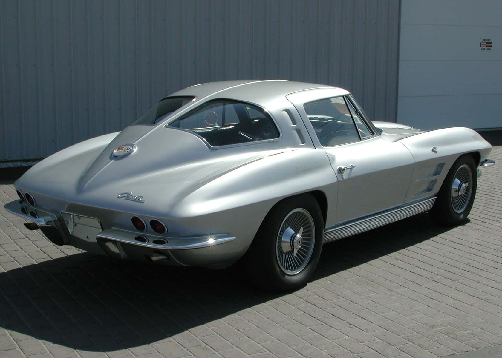 classic 桌布 壁紙 — 一輛時尚的銀色經典Corvette跑車停在鋪砌的磚面上，在明亮的日光下。