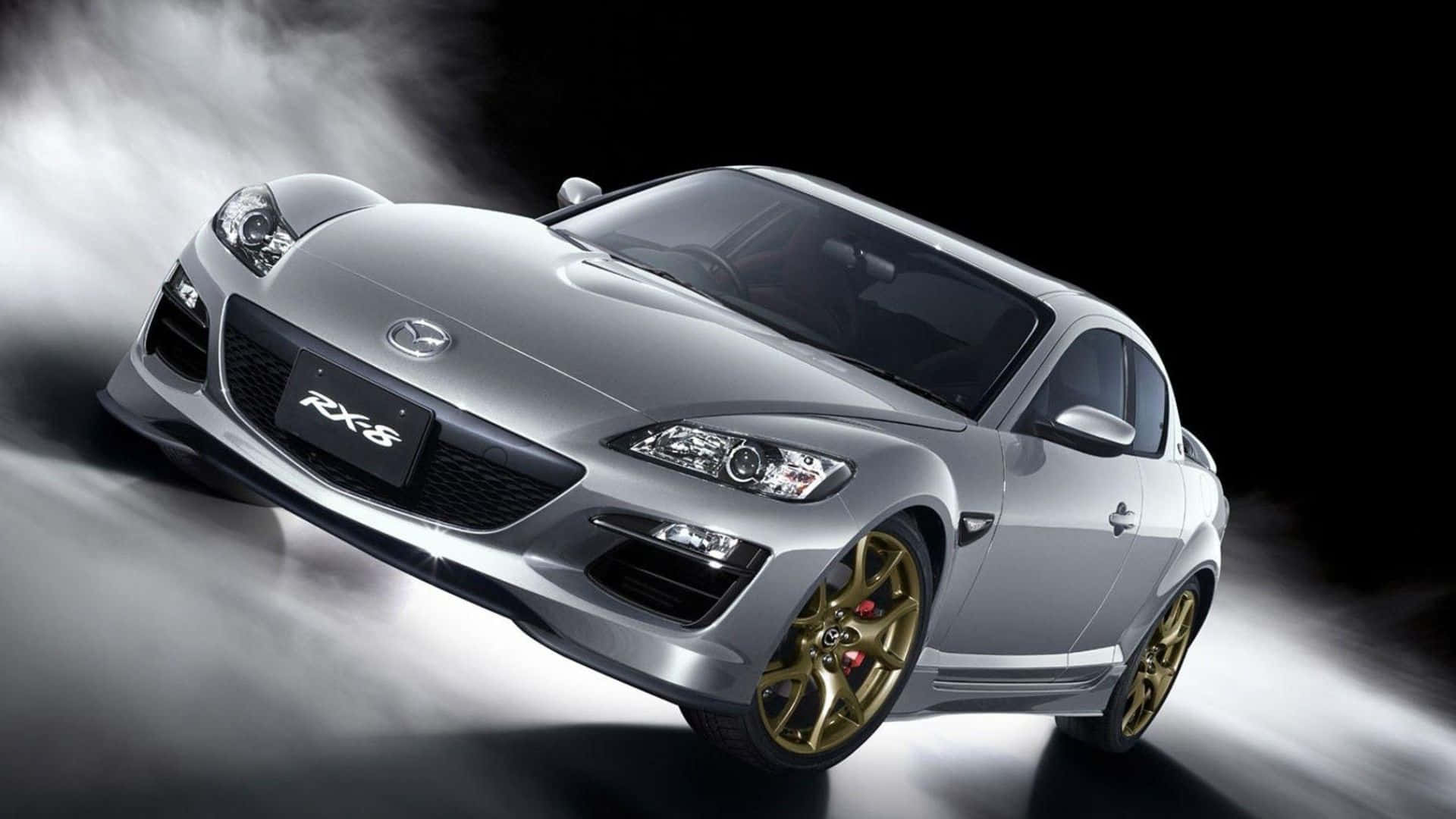 Mazda Rx-8 桌布 壁紙 — 一輛時尚的銀色萬事得RX-8跑車，配備金色輪圈和紅色制動卡鉗，在黑暗背景中穿過薄霧滑行。