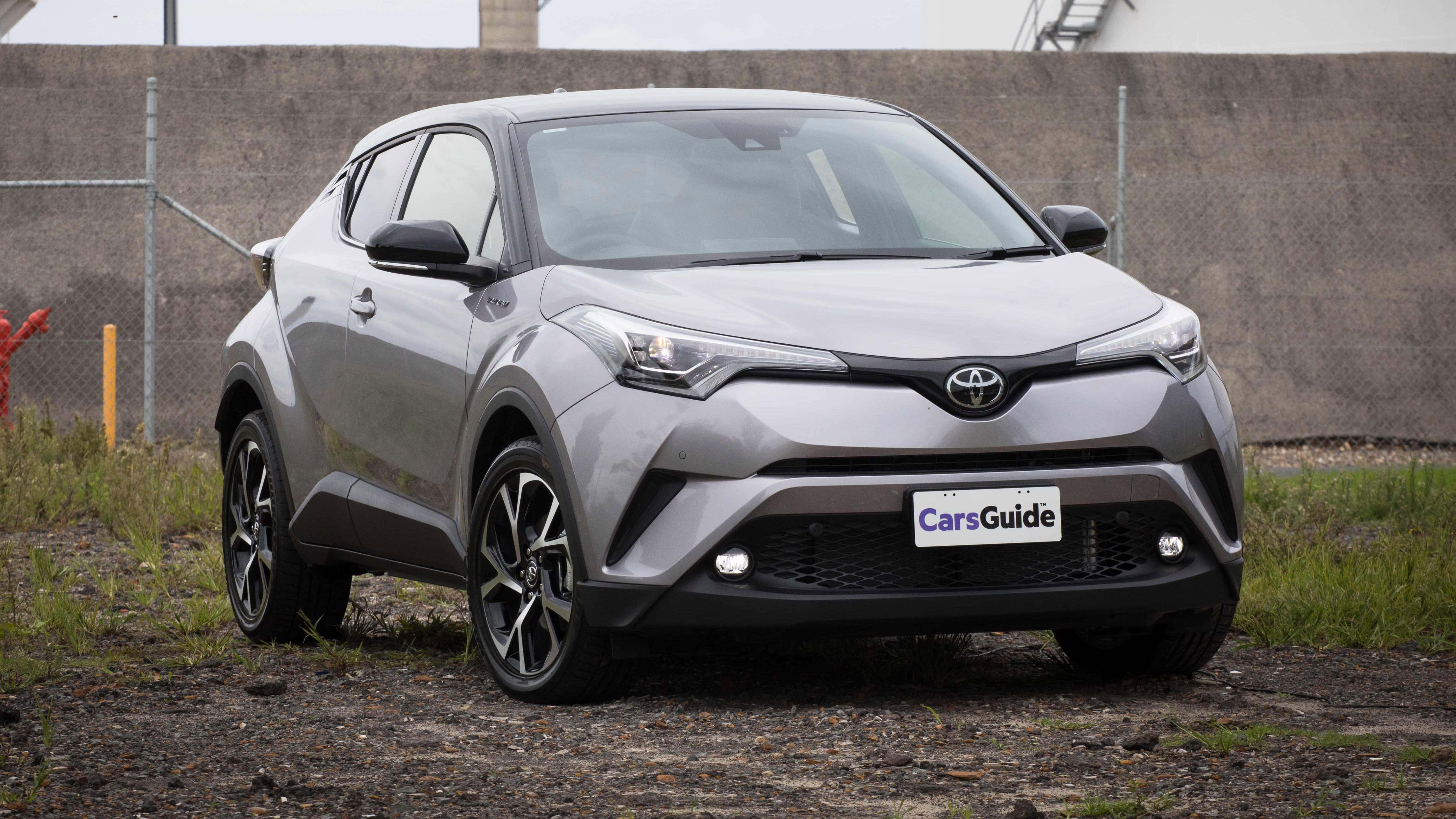 Compact Car 桌布 壁紙 — 一輛時尚的銀色豐田C-HR SUV停在碎石上，背景有鐵絲網圍欄和混凝土牆。