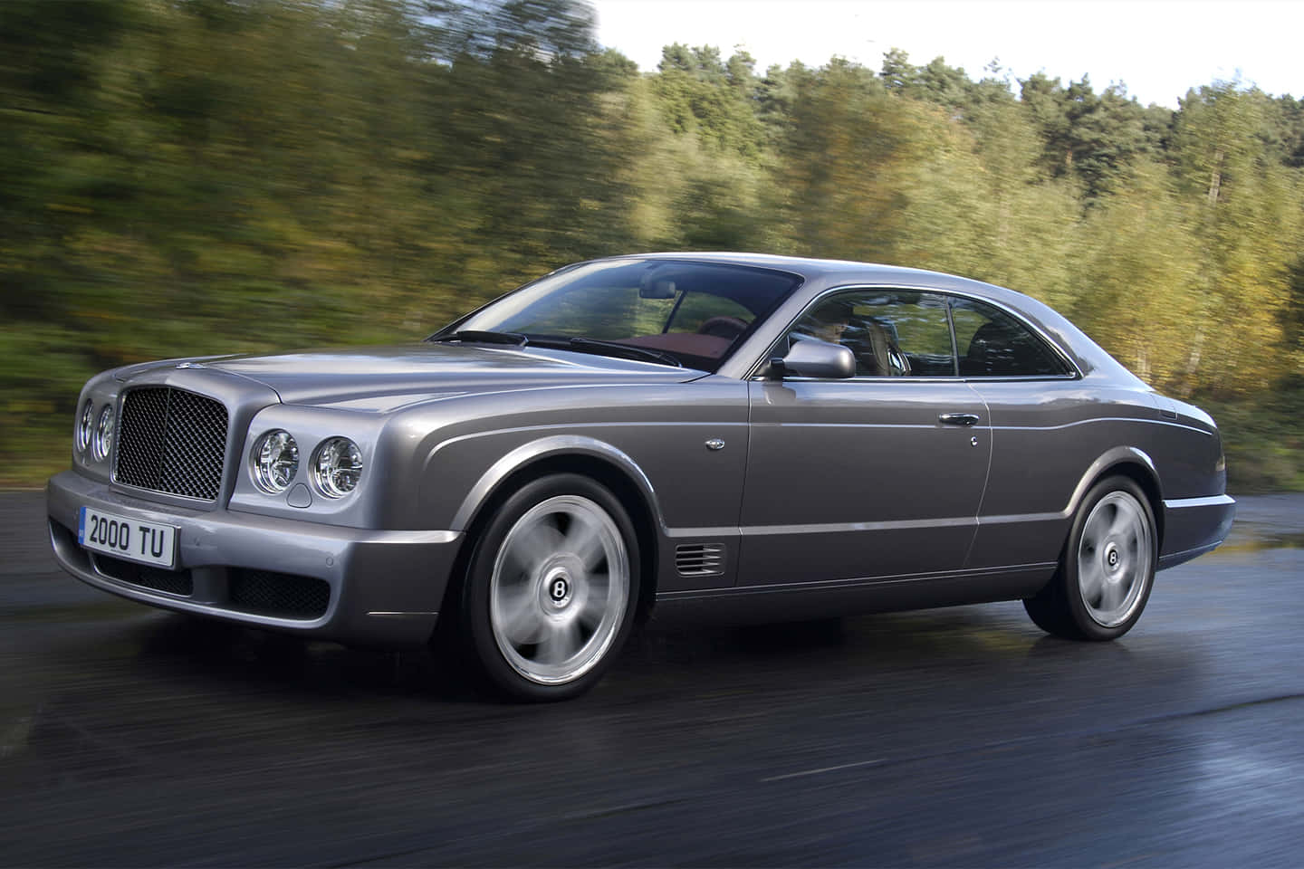 Bentley Brooklands 桌布 壁紙 — 一輛時尚的銀色賓利 Continental GT 在潮濕的道路上行駛，背景是模糊的秋樹。