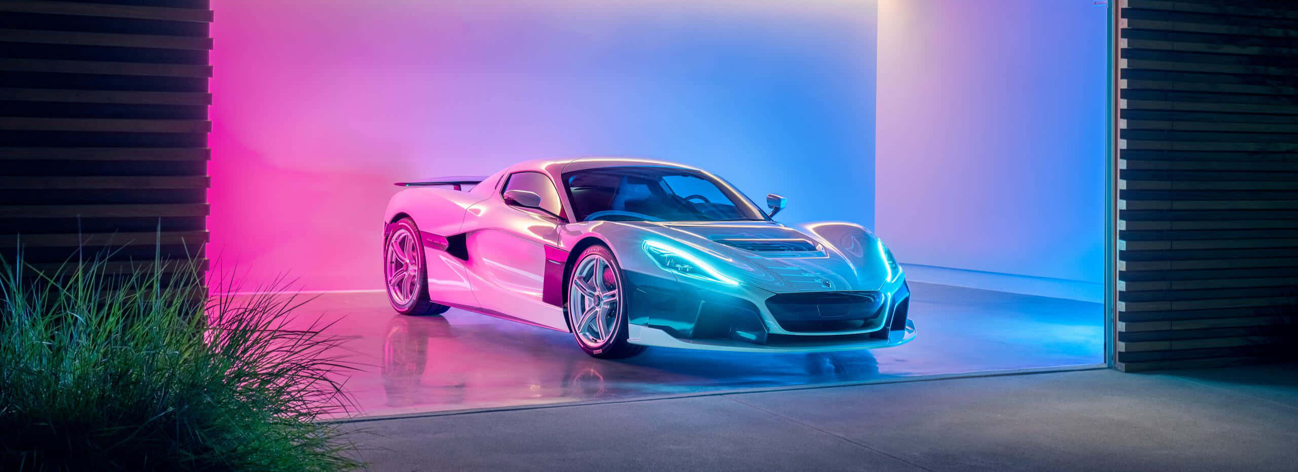 Rimac 桌布 壁紙 — 一輛時尚的銀色跑車在充滿活力的粉紅色和藍色霓虹燈下閃耀，位於一個現代化車庫內，外面有綠色植物。