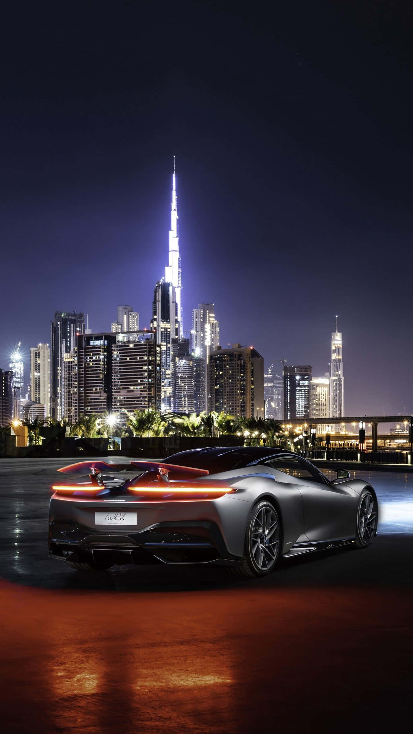 Pininfarina 桌布 壁紙 — 一輛時尚的銀色跑車在夜間杜拜璀璨的天際線襯托下，發出紅色尾燈的光芒。