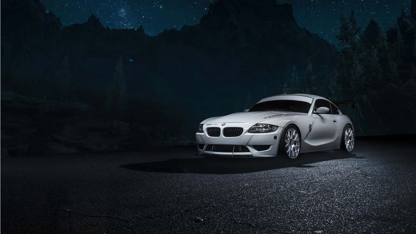 Bmw Z4 桌布 壁紙 — 一輛時尚的銀色跑車在星光下閃耀，停在夜間森林覆蓋的山脈旁黑暗的瀝青路上。