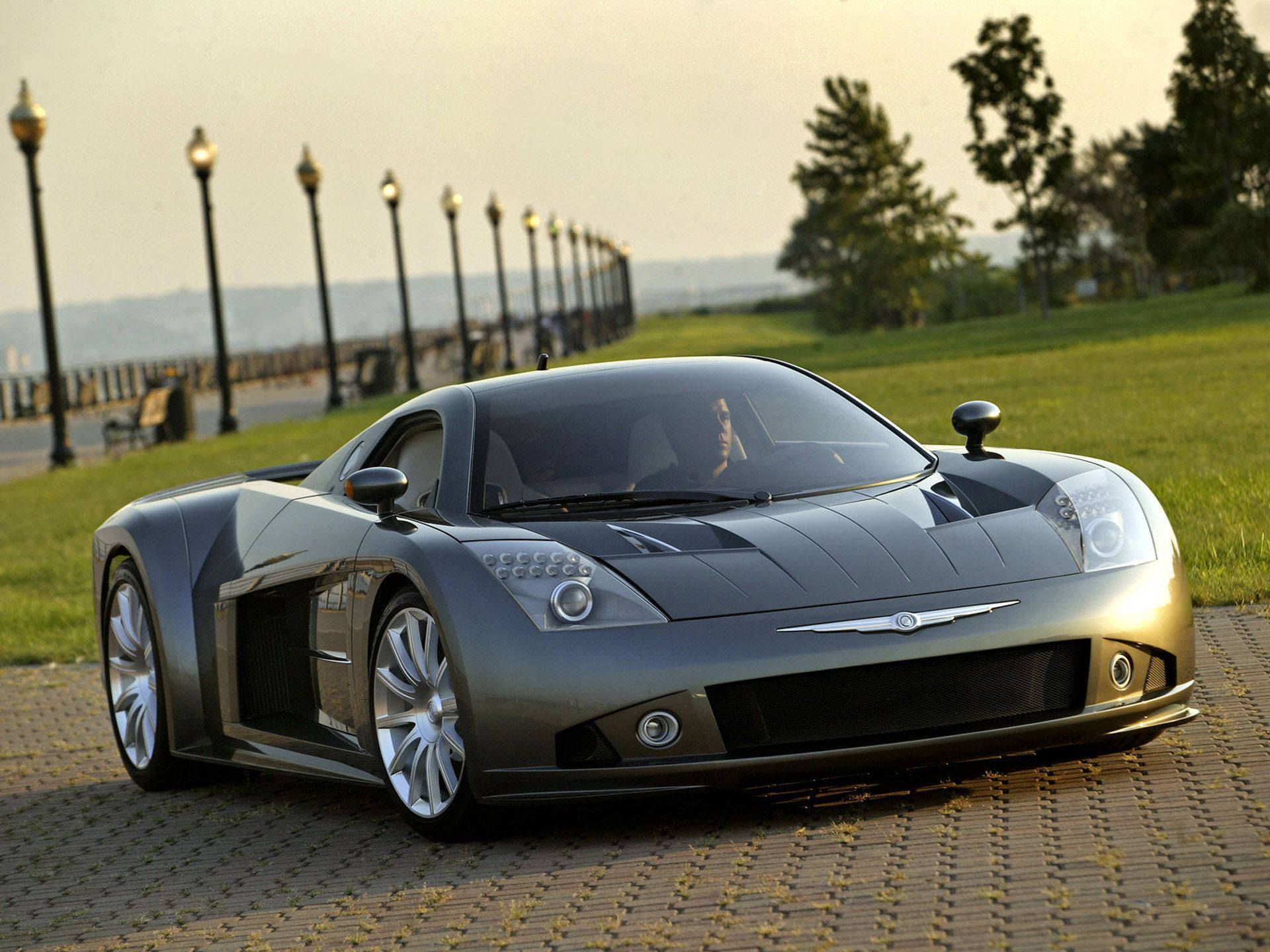 Chrysler ME Four-Twelve 壁紙 — 一輛時尚的銀色跑車在柔和的金色日落映照下，閃耀在公園旁鋪砌的小徑上，公園內有燈柱和樹木。