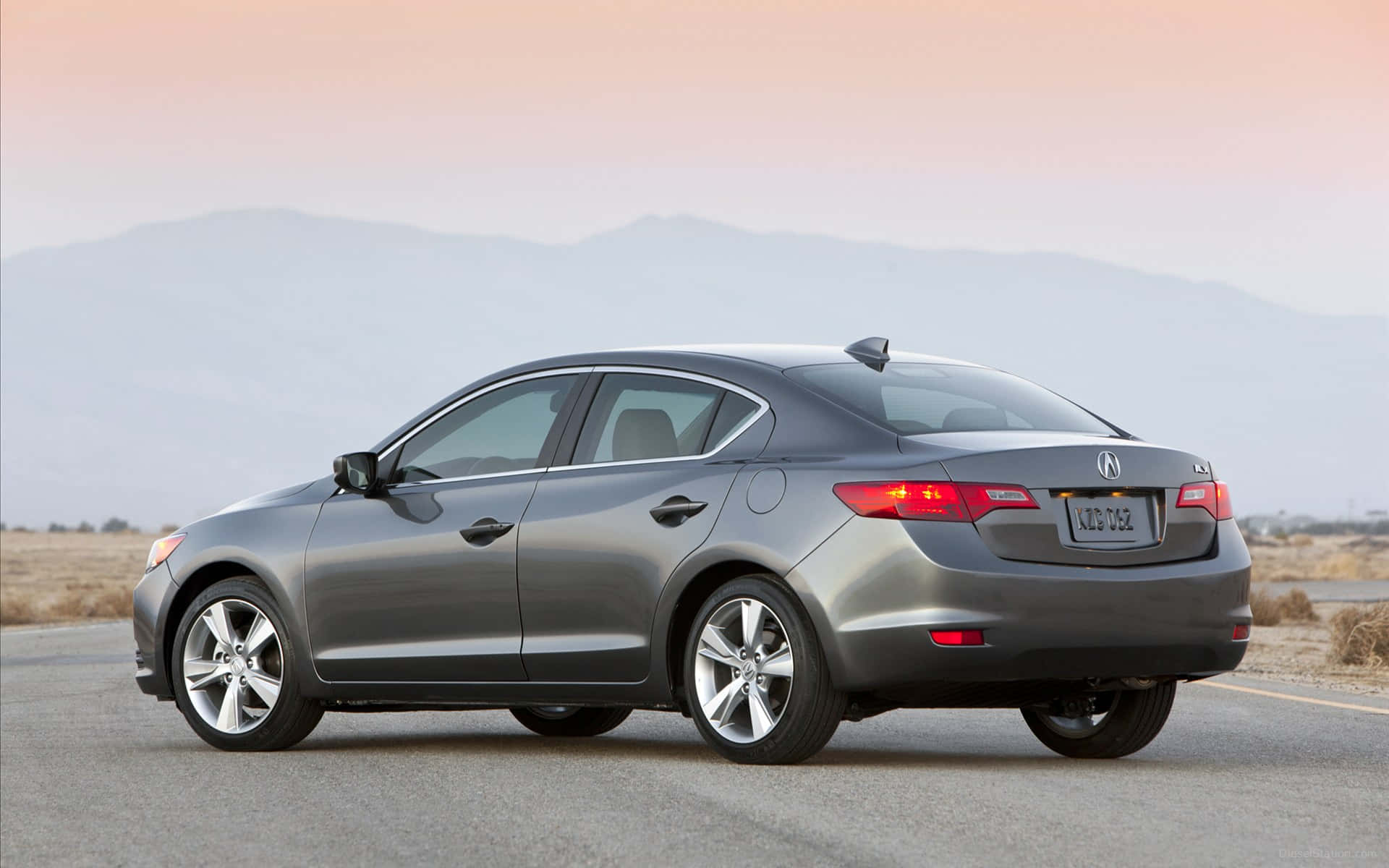 Acura Ilx 桌布 壁紙 — 一輛時尚的銀色轎車停在沙漠公路上，背景是夕陽下朦朧的山巒。