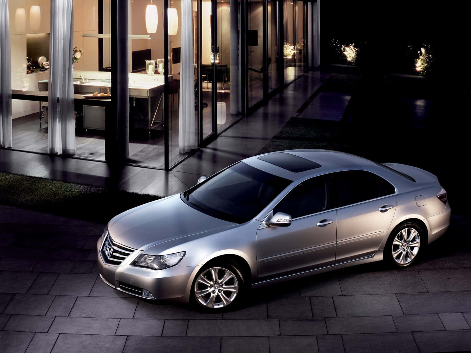 Honda Legend 桌布 壁紙 — 一輛時尚的銀色轎車停在現代玻璃屋外的石頭露台上，夜間室內燈光亮起。