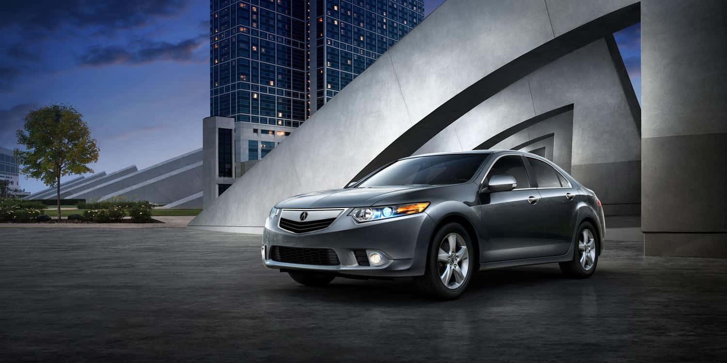 Acura Tsx 桌布 壁紙 — 一輛時尚的銀色轎車停泊在現代混凝土拱門下，背後有玻璃摩天大樓在黃昏中發光。