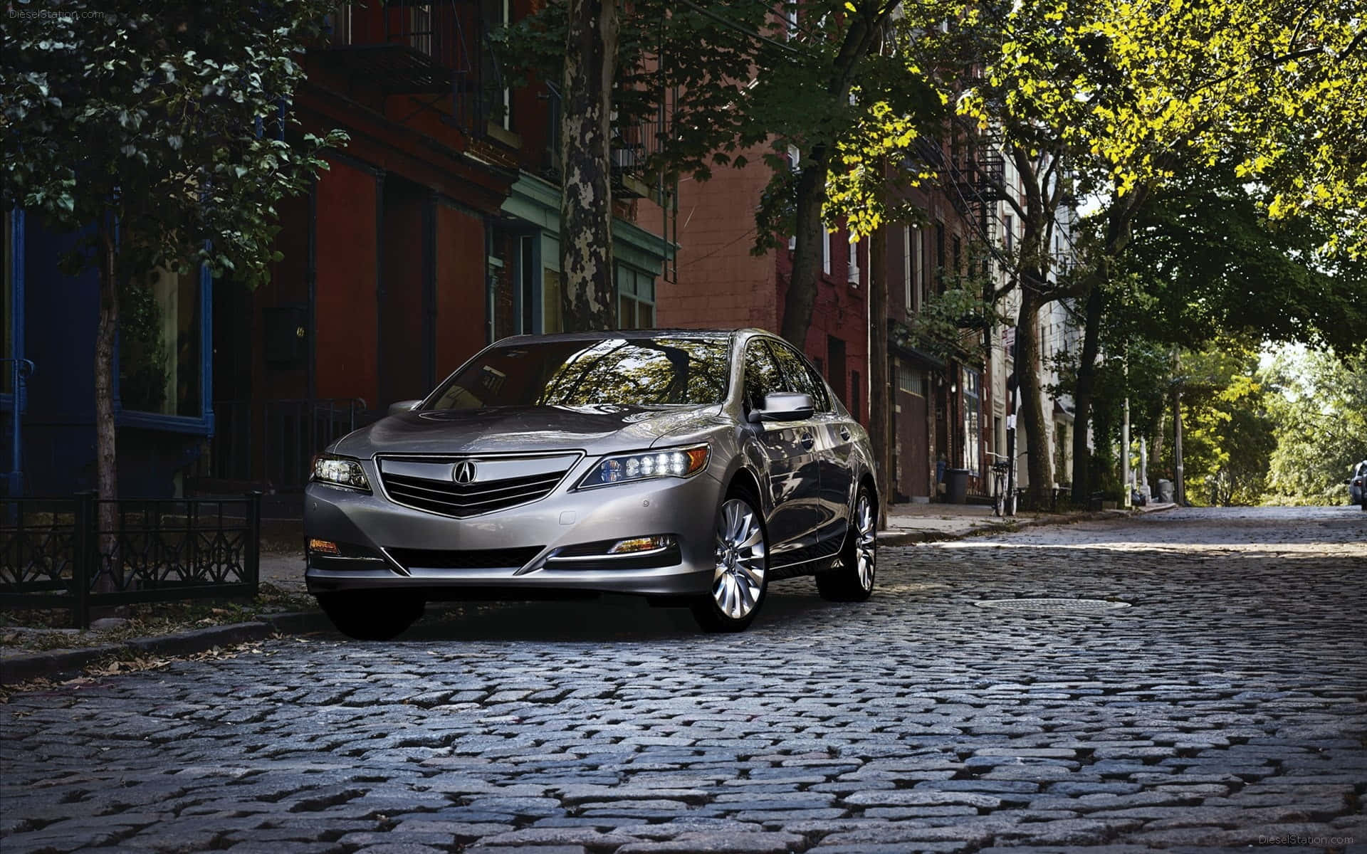 Acura Rlx 桌布 壁紙 — 一輛時尚的銀色轎車停泊在綠樹成蔭的鵝卵石街道上，兩旁是磚砌建築，陽光斑駁。