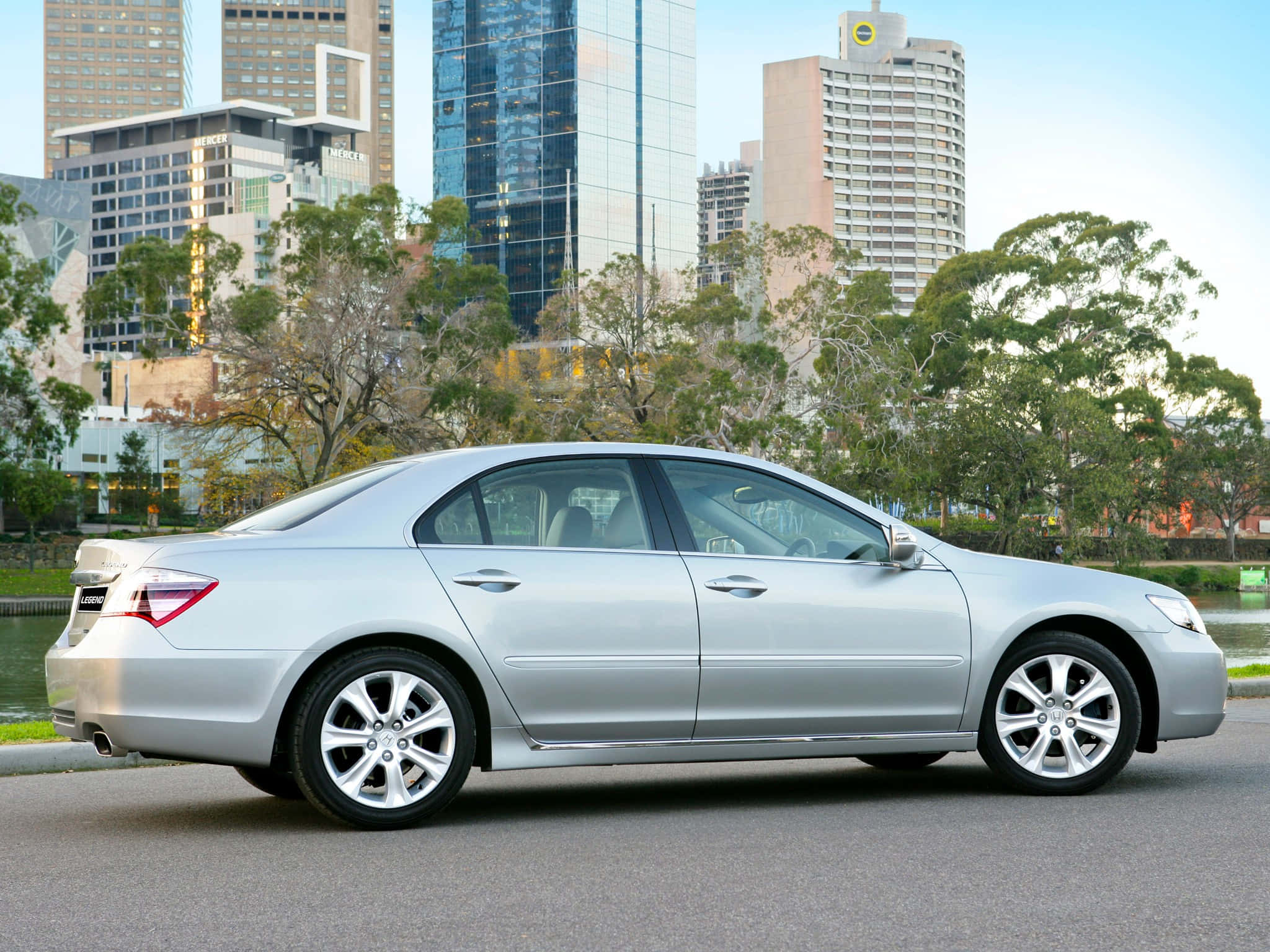 Honda Legend 桌布 壁紙 — 一輛時尚的銀色轎車停泊在都市街道上，背景是現代摩天大樓和綠樹。