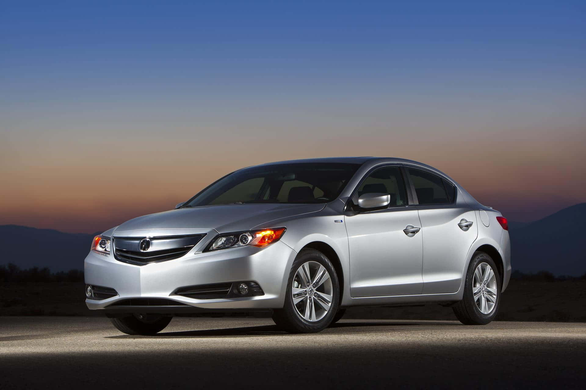 Acura Ilx 桌布 壁紙 — 一輛時尚的銀色轎車在暮色天空下閃閃發光，遠處有山巒。