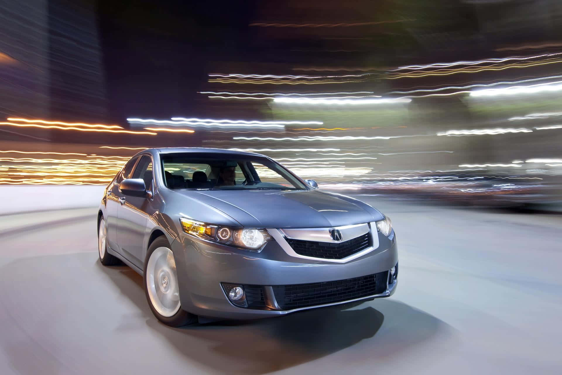 Acura Tsx 桌布 壁紙 — 一輛時尚的銀色轎車在模糊的夜間城市景觀中疾馳，身後留下條狀燈光。