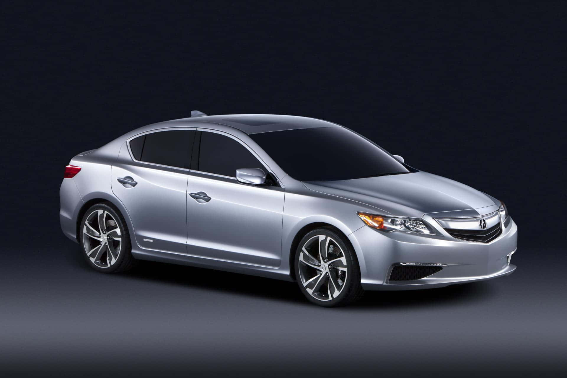 Acura Ilx 桌布 壁紙 — 一輛時尚的銀色轎車配備合金輪圈，在黑暗的攝影棚背景下以戲劇性燈光展示。