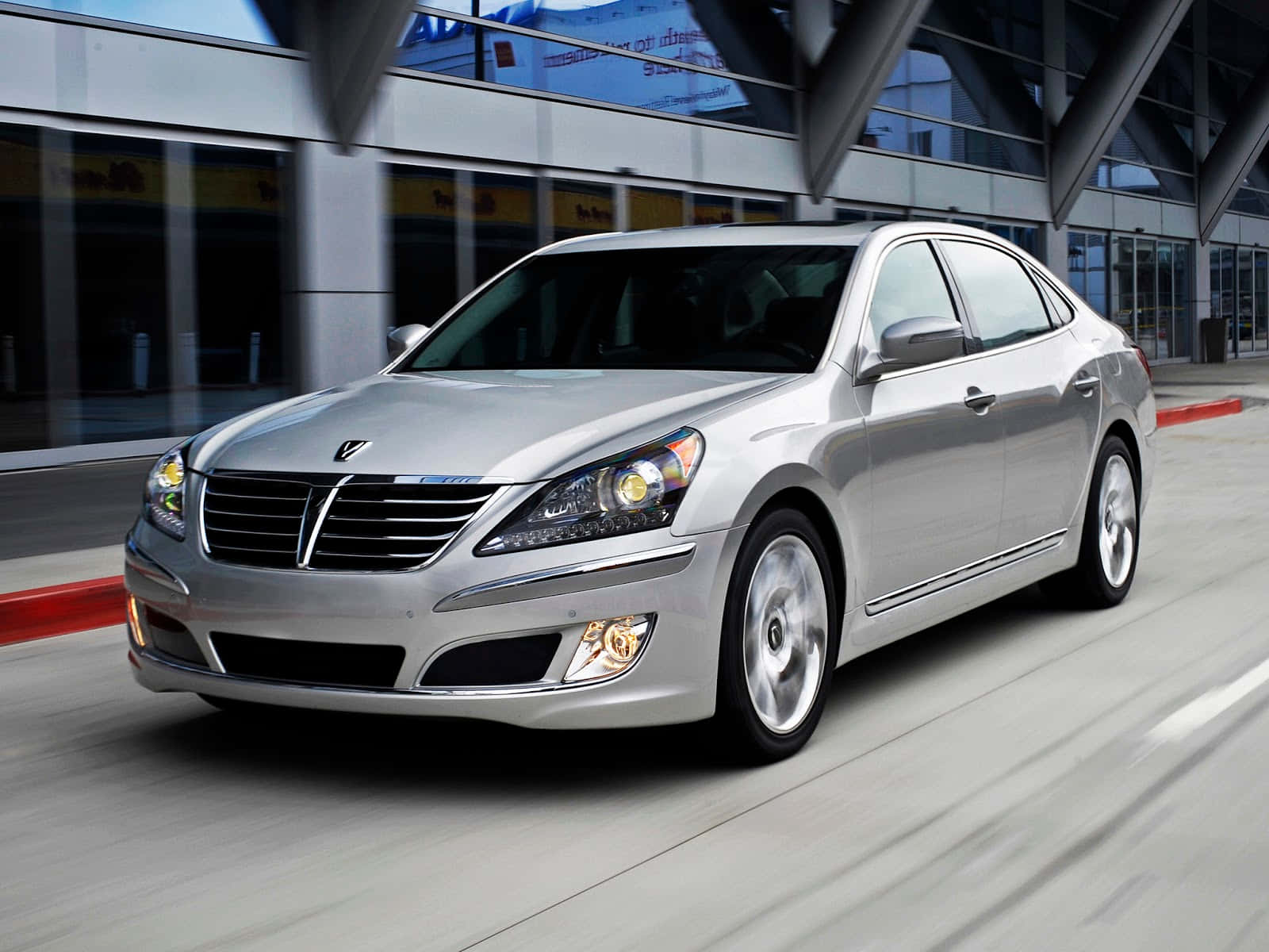 Hyundai Equus 桌布 壁紙 — 一輛時尚的銀色轎車駛過現代玻璃建築，人行道上留下動態模糊效果。