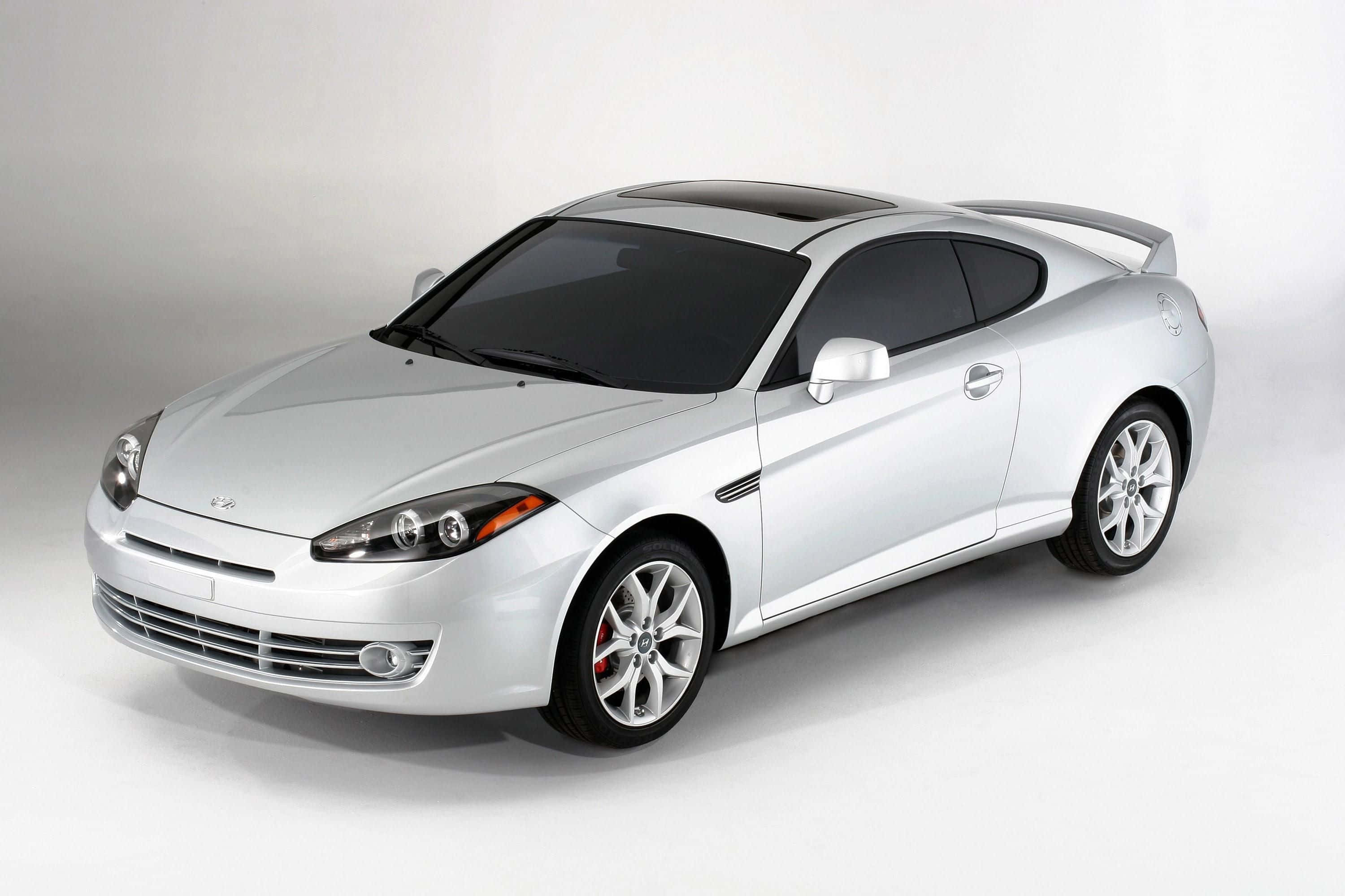 Hyundai Tiburon 桌布 壁紙 — 一輛時尚的銀色運動轎跑車，帶有黑色飾件和紅色制動卡鉗，在乾淨的白色工作室背景前擺拍。