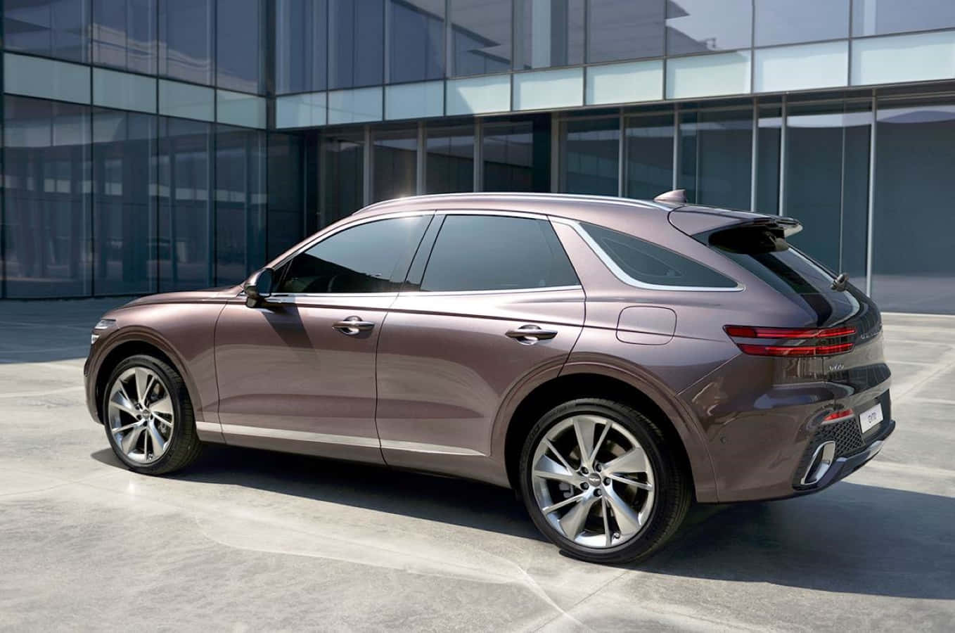Genesis Gv70 桌布 壁紙 — 一輛時尚的銅色SUV在明亮的日光下停泊在現代玻璃建築前。