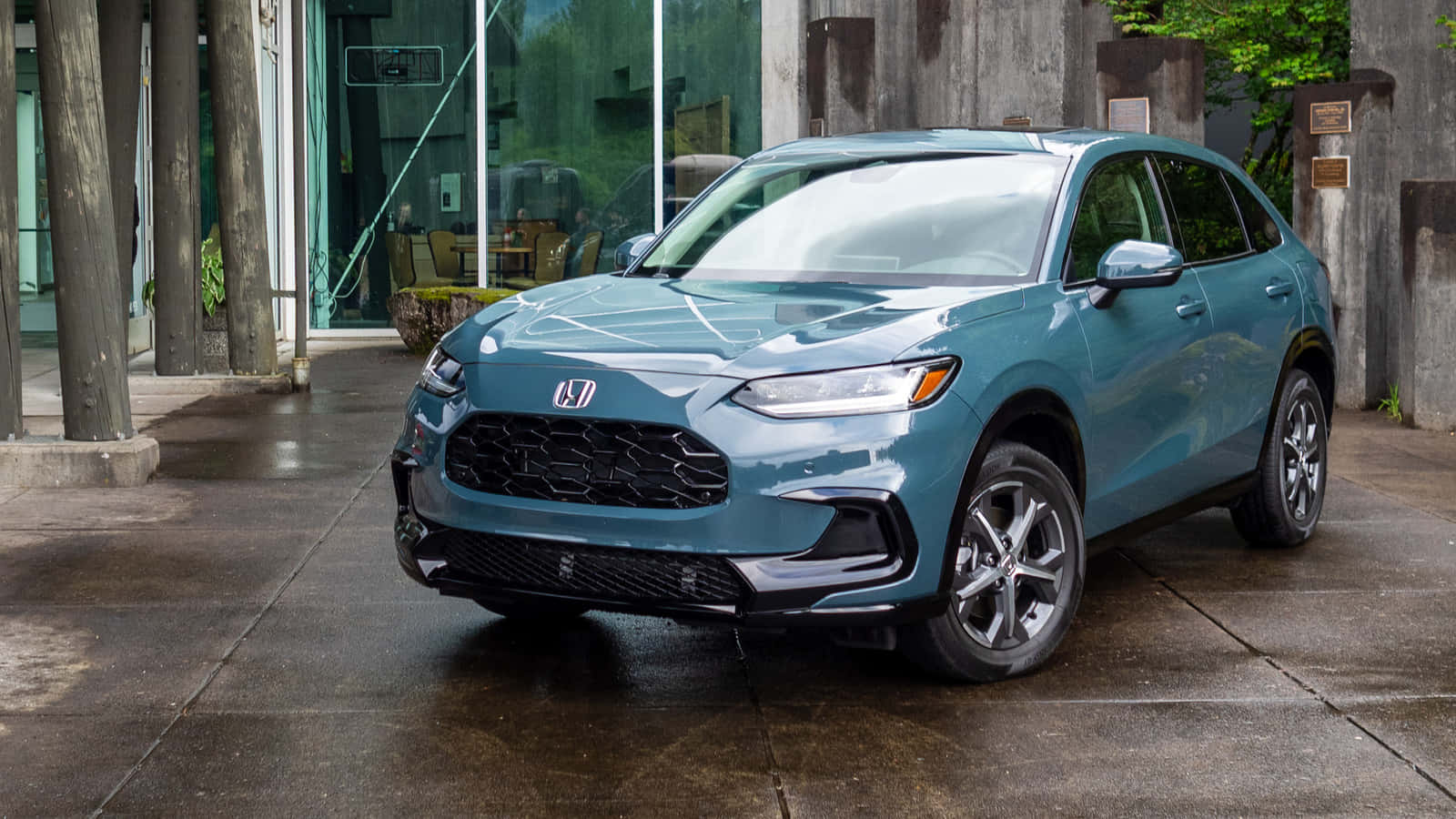 Honda Hr-v 桌布 壁紙 — 一輛時尚的青綠色本田SUV停泊在濕漉漉的混凝土車道上，旁邊是現代玻璃建築，背景有樹木。