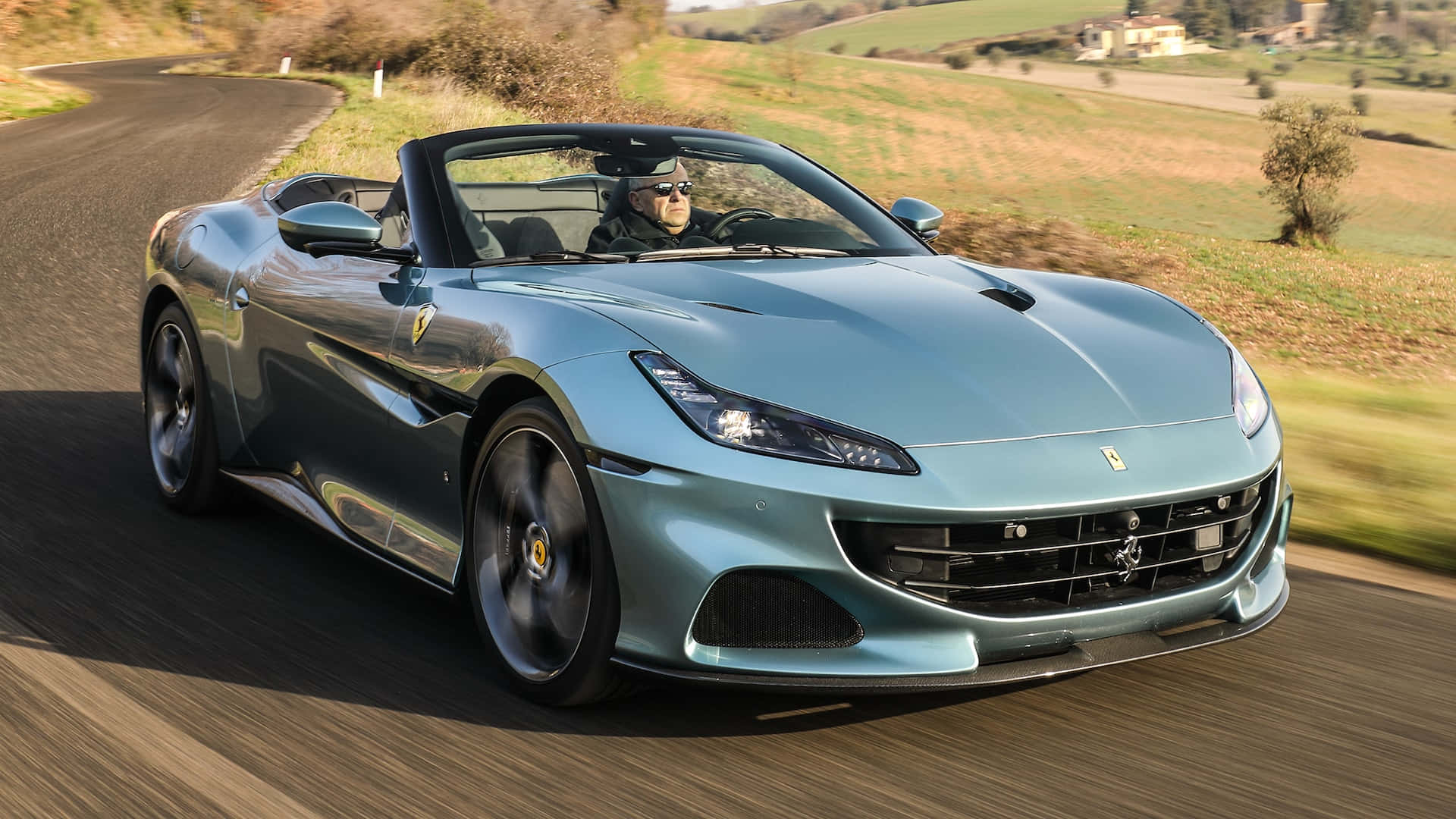 Ferrari Portofino 桌布 壁紙 — 一輛時尚的青綠色法拉利敞篷車在蜿蜒的鄉間道路上疾馳，司機戴著太陽眼鏡。