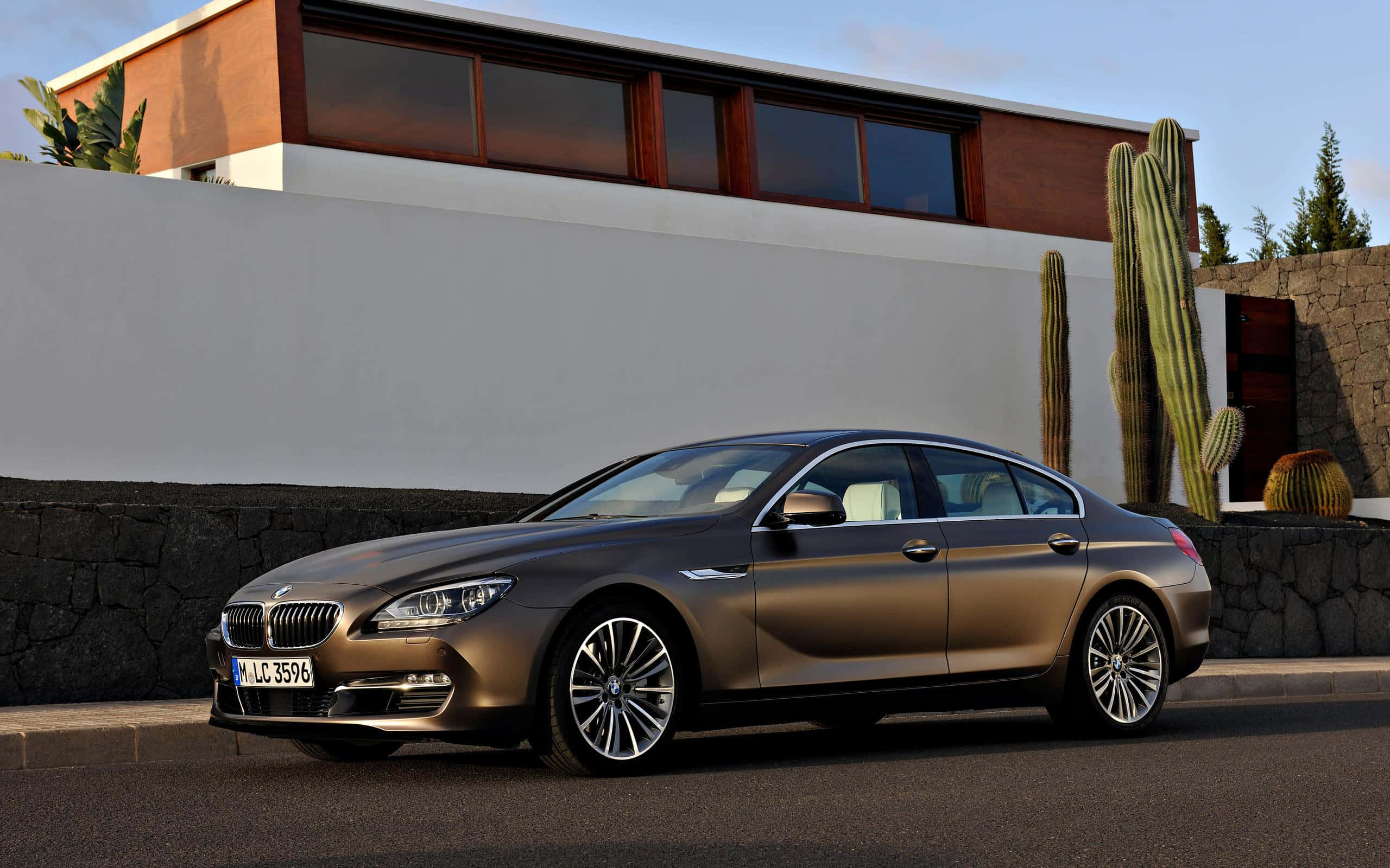 Bmw 6 Series 桌布 壁紙 — 一輛時尚的青銅色BMW 6系轎車停在瀝青路上，旁邊是現代住宅，有仙人掌和石牆，天空晴朗。