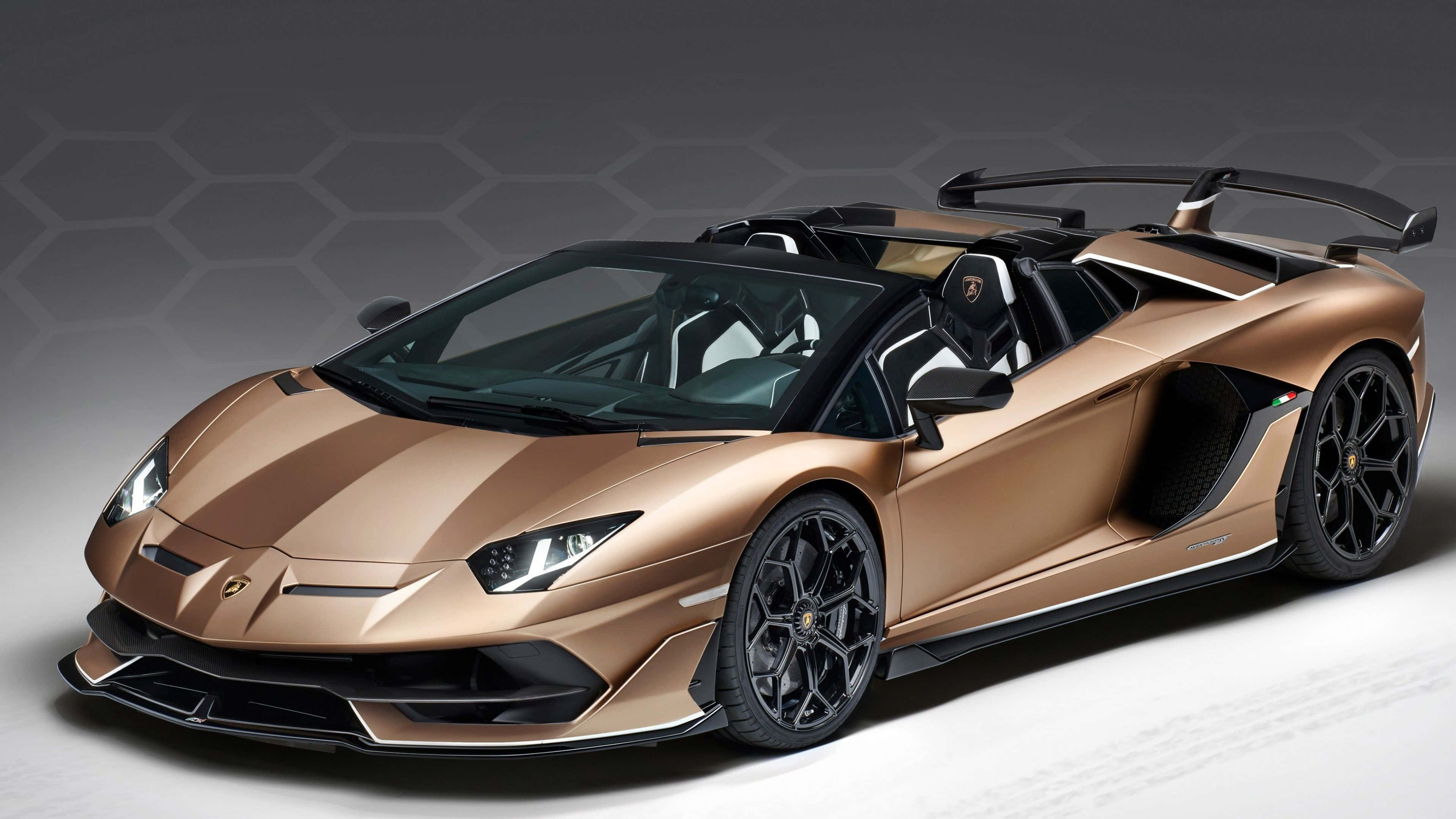 林寶堅尼 4K 桌布 壁紙 — 一輛時尚的青銅色林寶堅尼 Aventador SVJ Roadster，帶有黑色飾邊和突出的尾翼，在六邊形圖案的灰色工作室背景前擺拍。