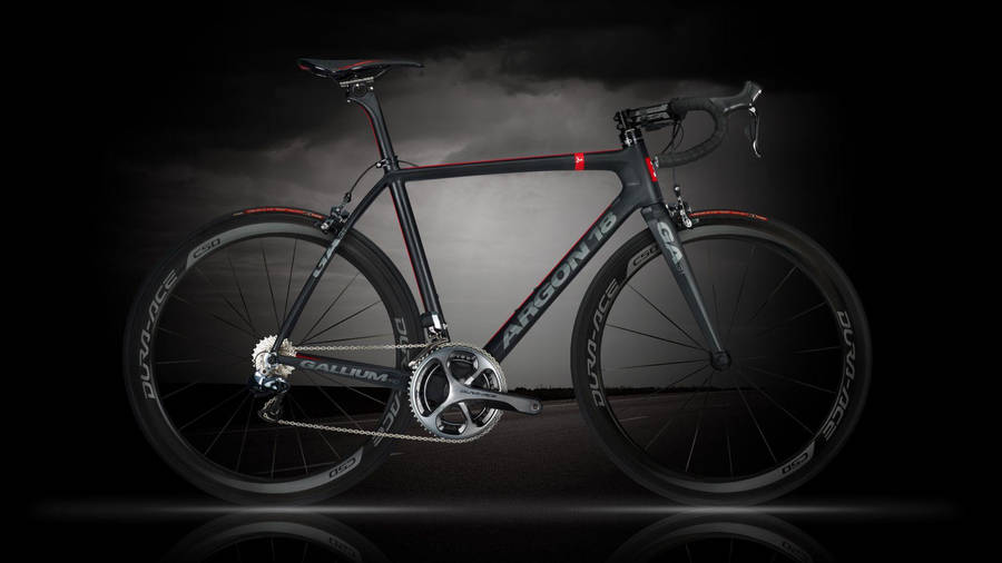 桌布 壁紙 — 一輛時尚的黑色 Argon 18 公路單車，帶有紅色點綴，在暴風雨般的灰色天空背景下戲劇性地矗立。