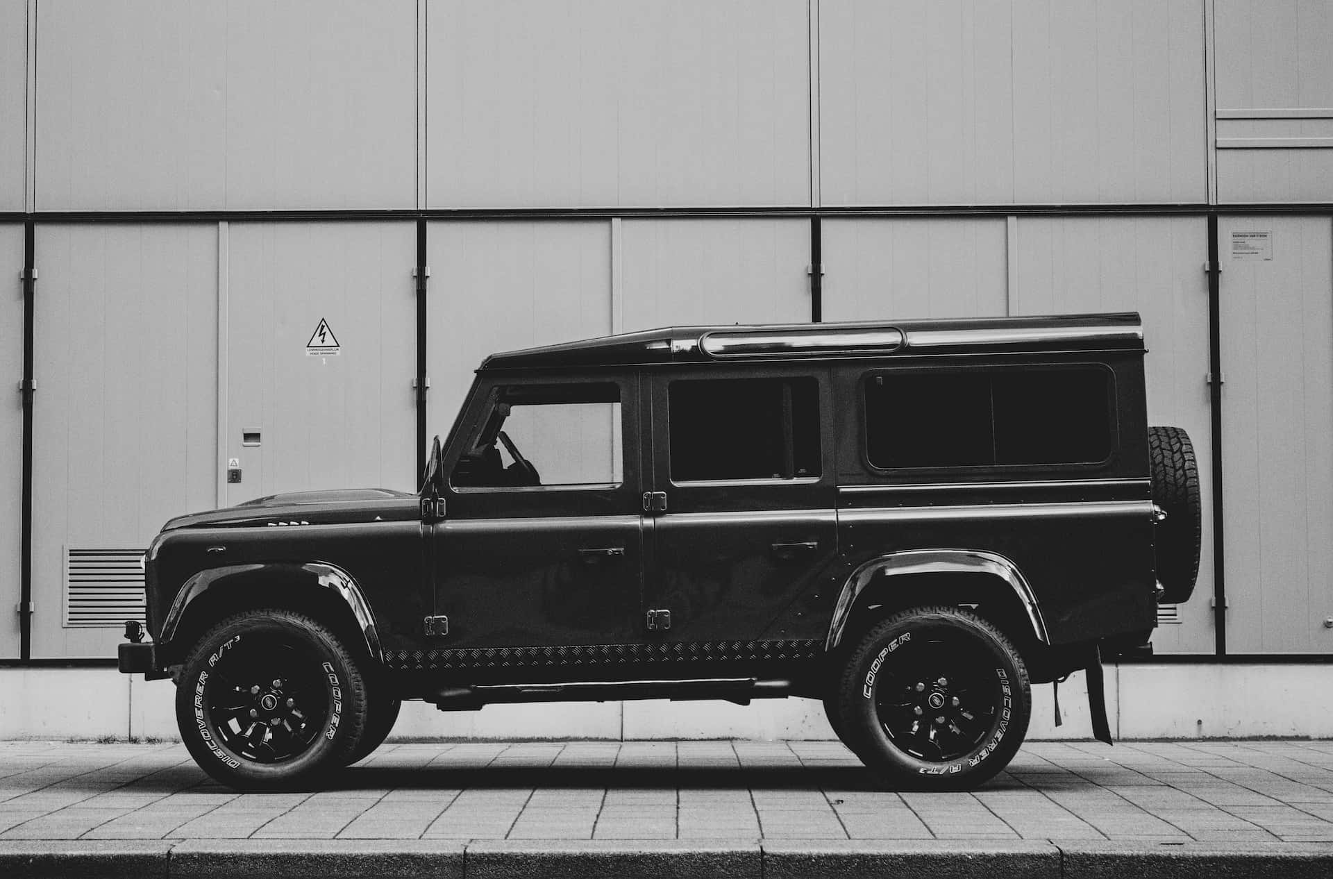 Black And White Car 桌布 壁紙 — 一輛時尚的黑色 Land Rover Defender 停在一棟極簡工業建築前，呈現單色調。