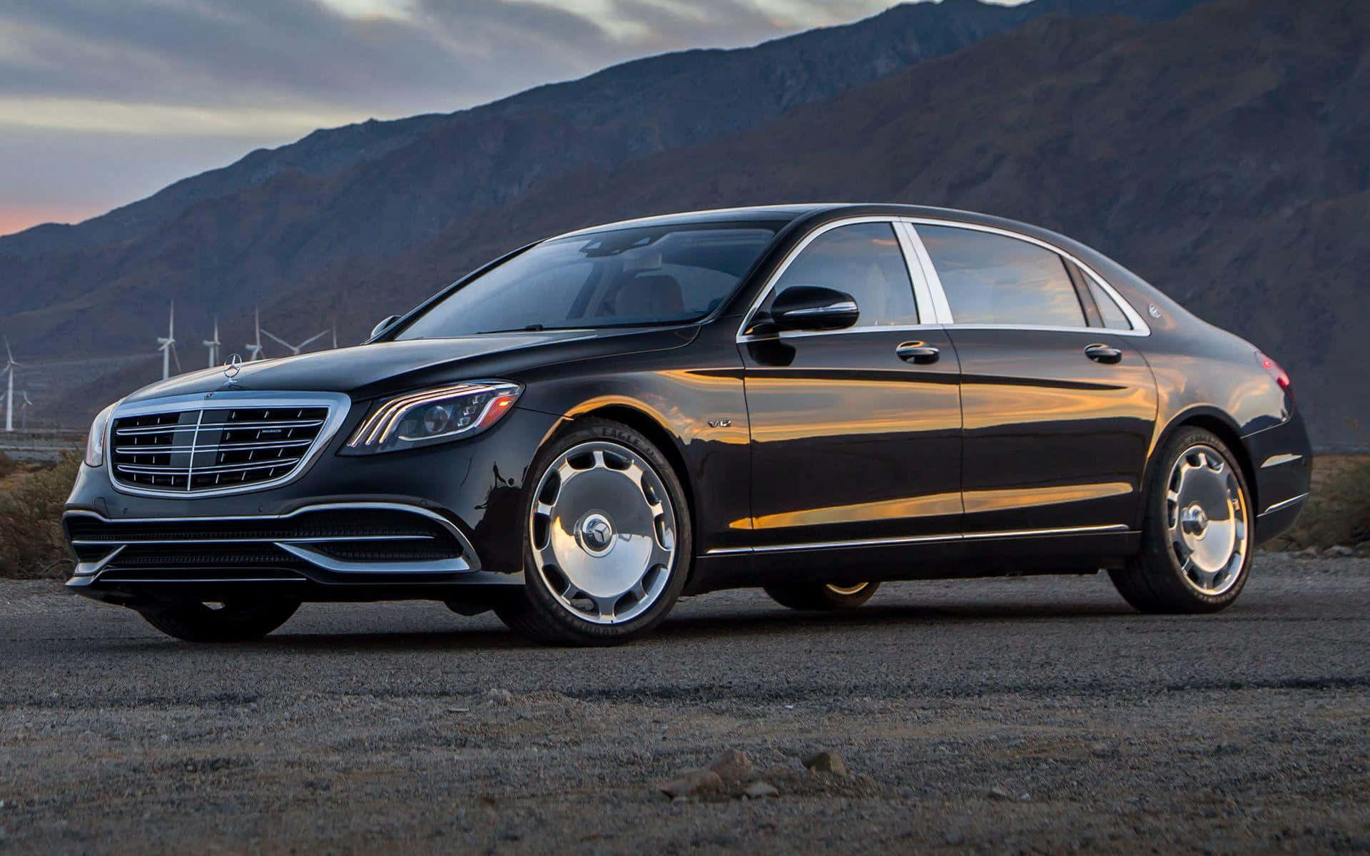 Maybach 桌布 壁紙 — 一輛時尚的黑色 Mercedes-Maybach S-Class 轎車在金色日落光芒下閃耀，背景是山巒和風力發電機。
