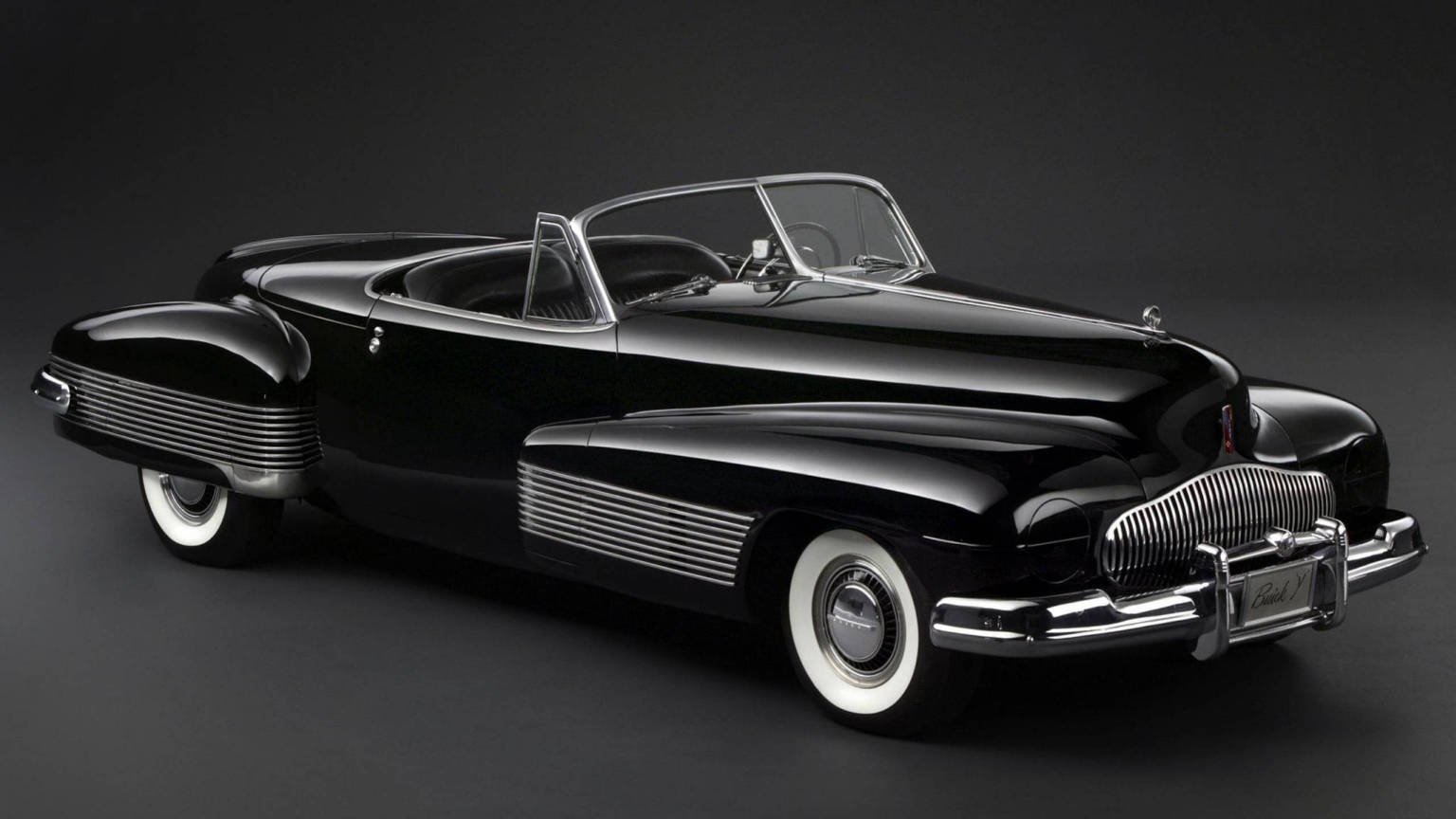 Vintage Car 桌布 壁紙 — 一輛時尚的黑色1940年代敞篷車，帶有鍍鉻裝飾和白色側壁輪胎，在攝影棚燈光下閃閃發光。