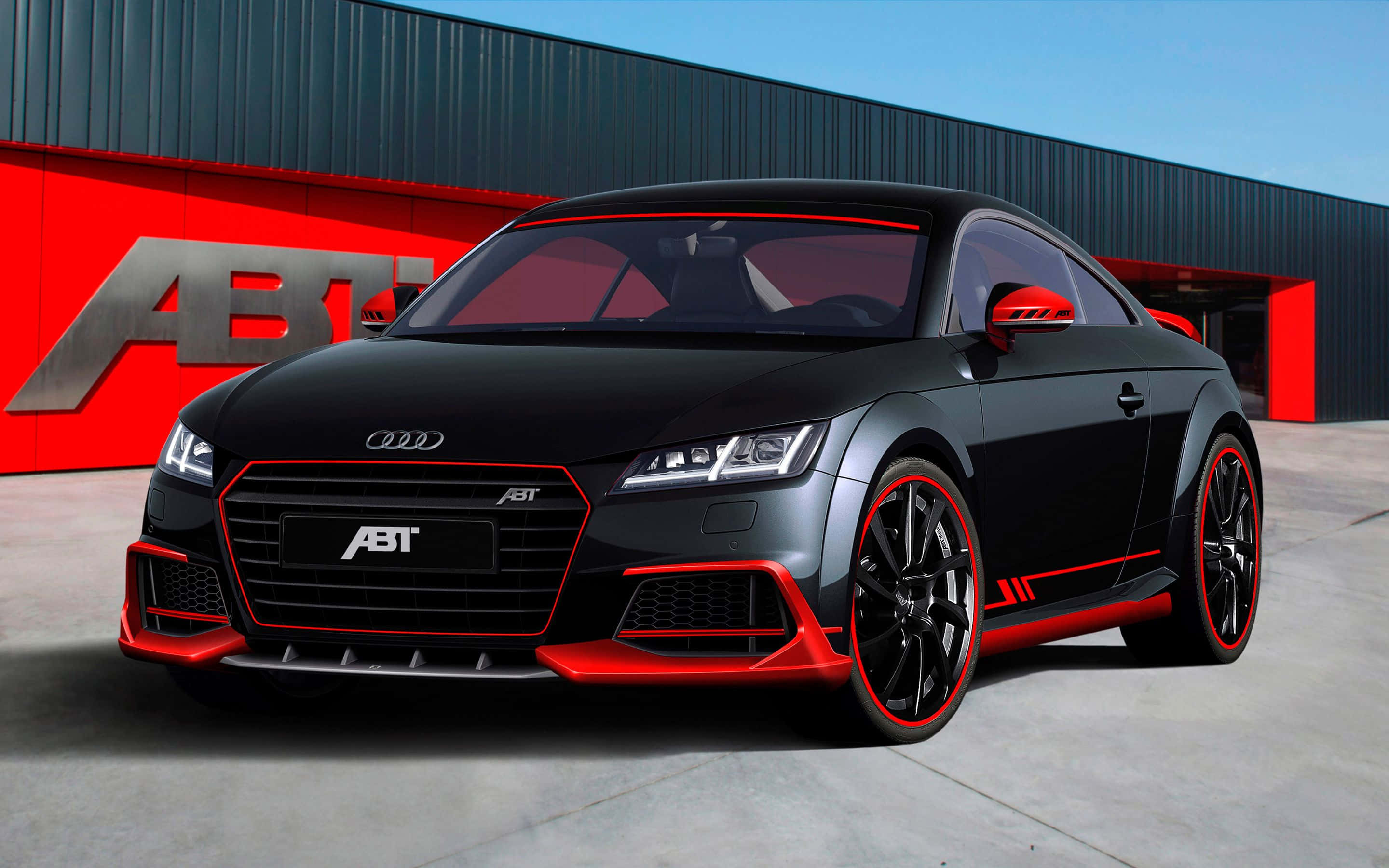 Audi Tt 桌布 壁紙 — 一輛時尚的黑色ABT Audi TT帶有醒目紅色點綴，在晴朗藍天下停在一座紅黑相間的工業建築前。