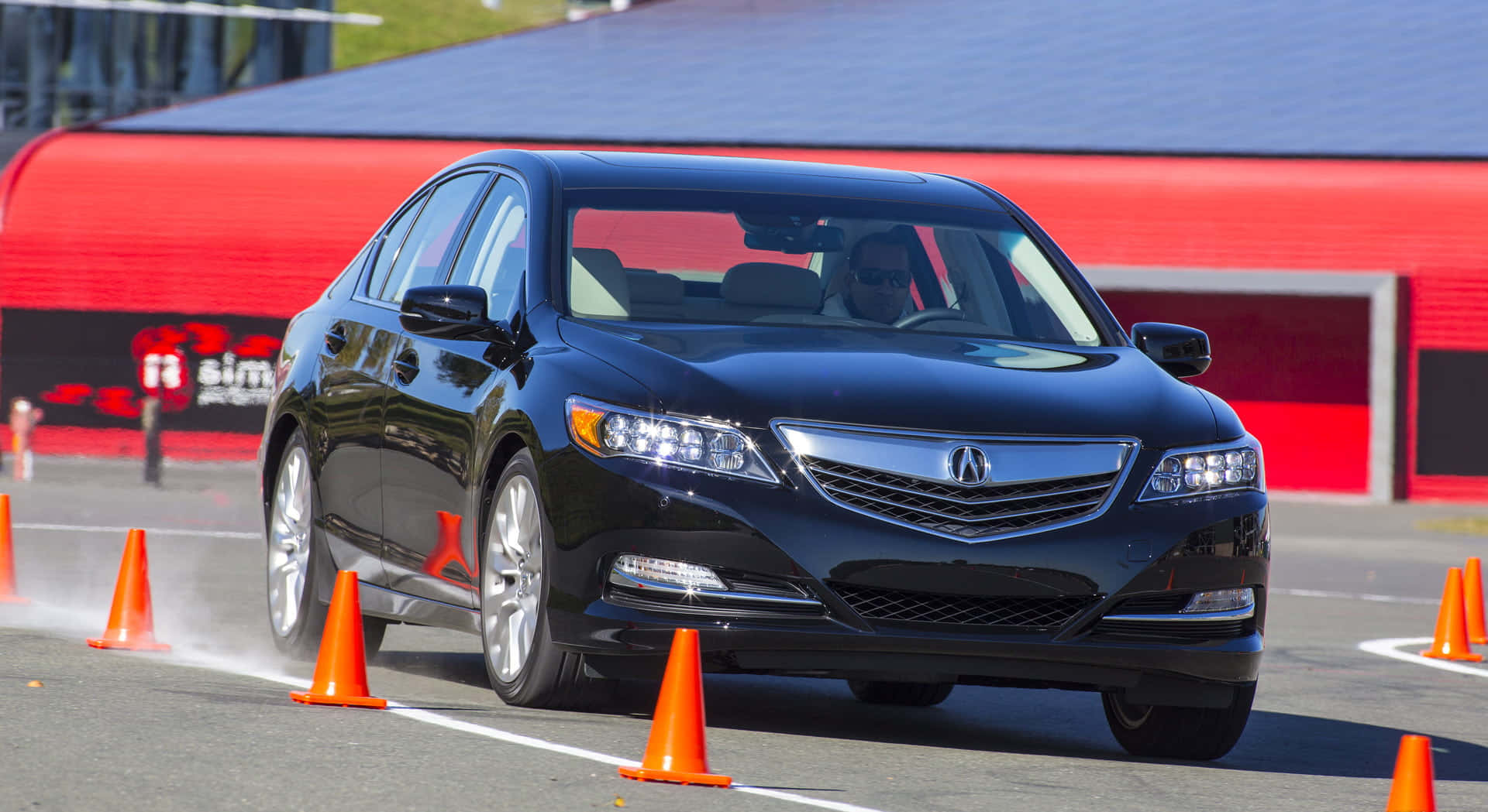 Acura Rlx 桌布 壁紙 — 一輛時尚的黑色Acura房車在明亮的日光下，在賽道上繞過橙色錐體進行急轉彎。