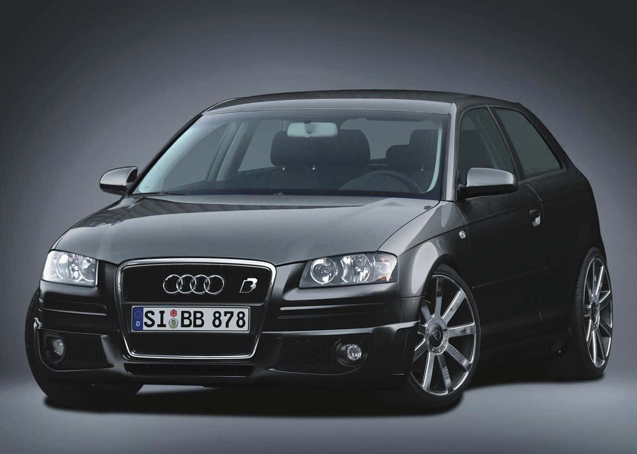 Audi A3 桌布 壁紙 — 一輛時尚的黑色Audi B4跑車，配備銀色輪圈和發光車頭燈，在深色漸變工作室背景前擺拍。