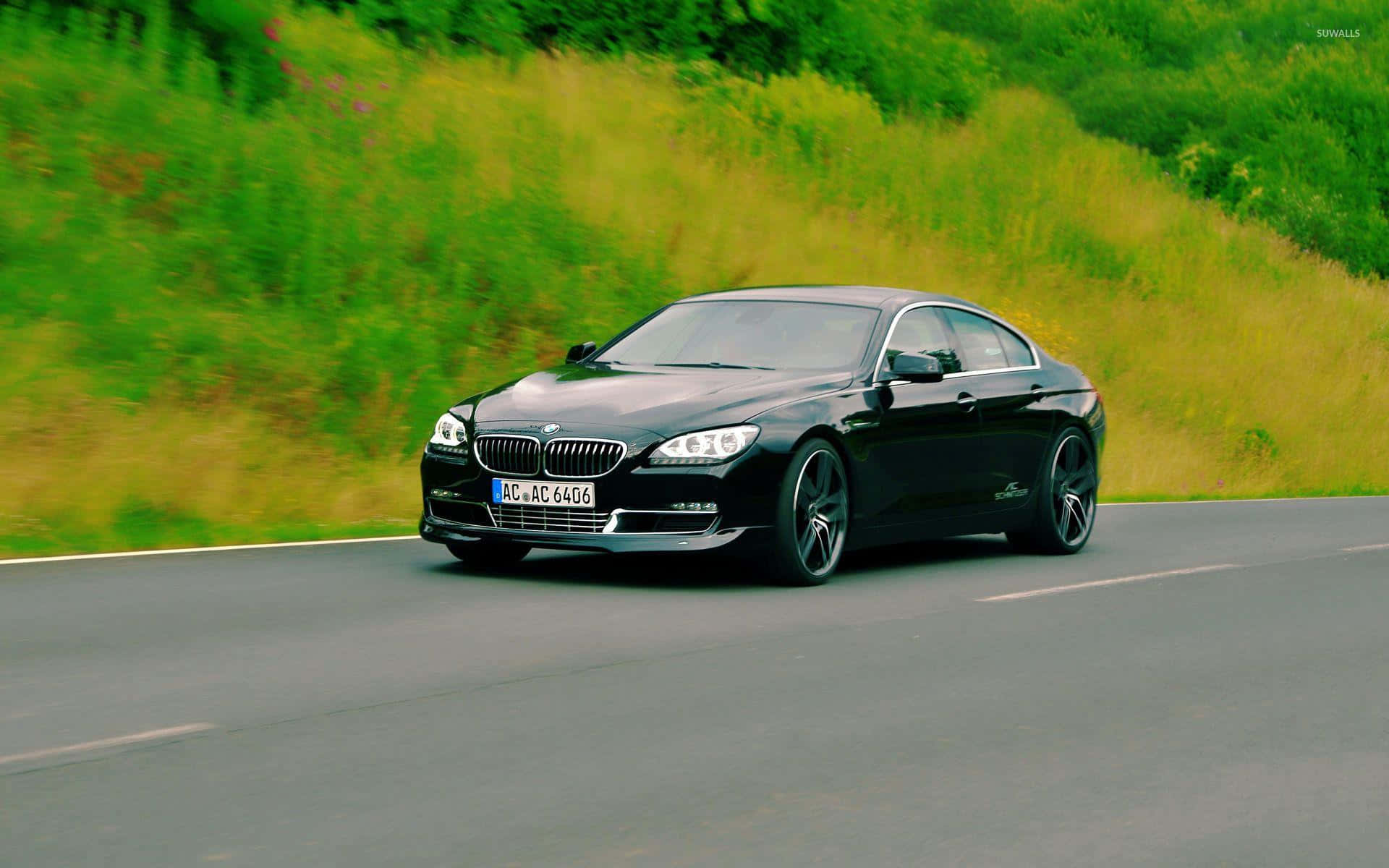 Bmw 6 Series 桌布 壁紙 — 一輛時尚的黑色BMW 6系轎跑車在蜿蜒的道路上疾馳，道路兩旁是充滿活力的綠色和黃色草地。