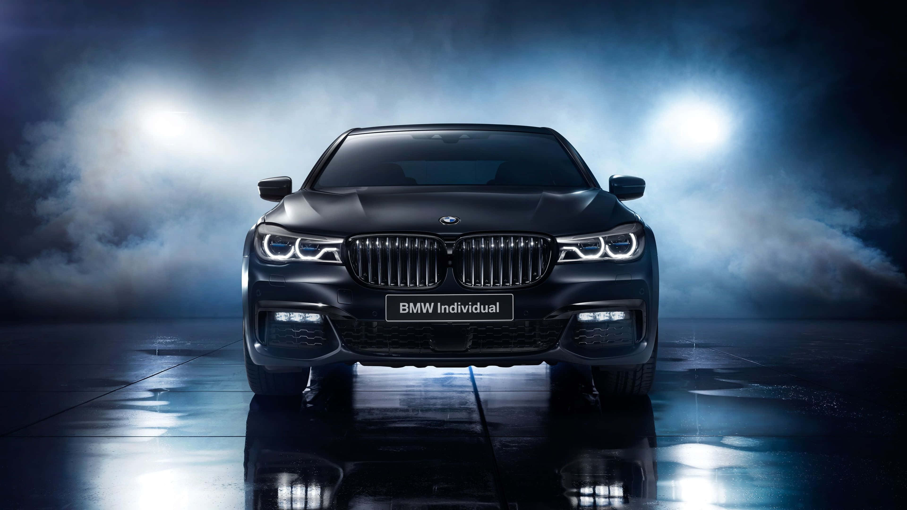 4K BMW 壁紙 桌布 壁紙 — 一輛時尚的黑色BMW Individual轎車在戲劇性的聚光燈和薄霧下，面向前方，停在反光的濕滑地板上。