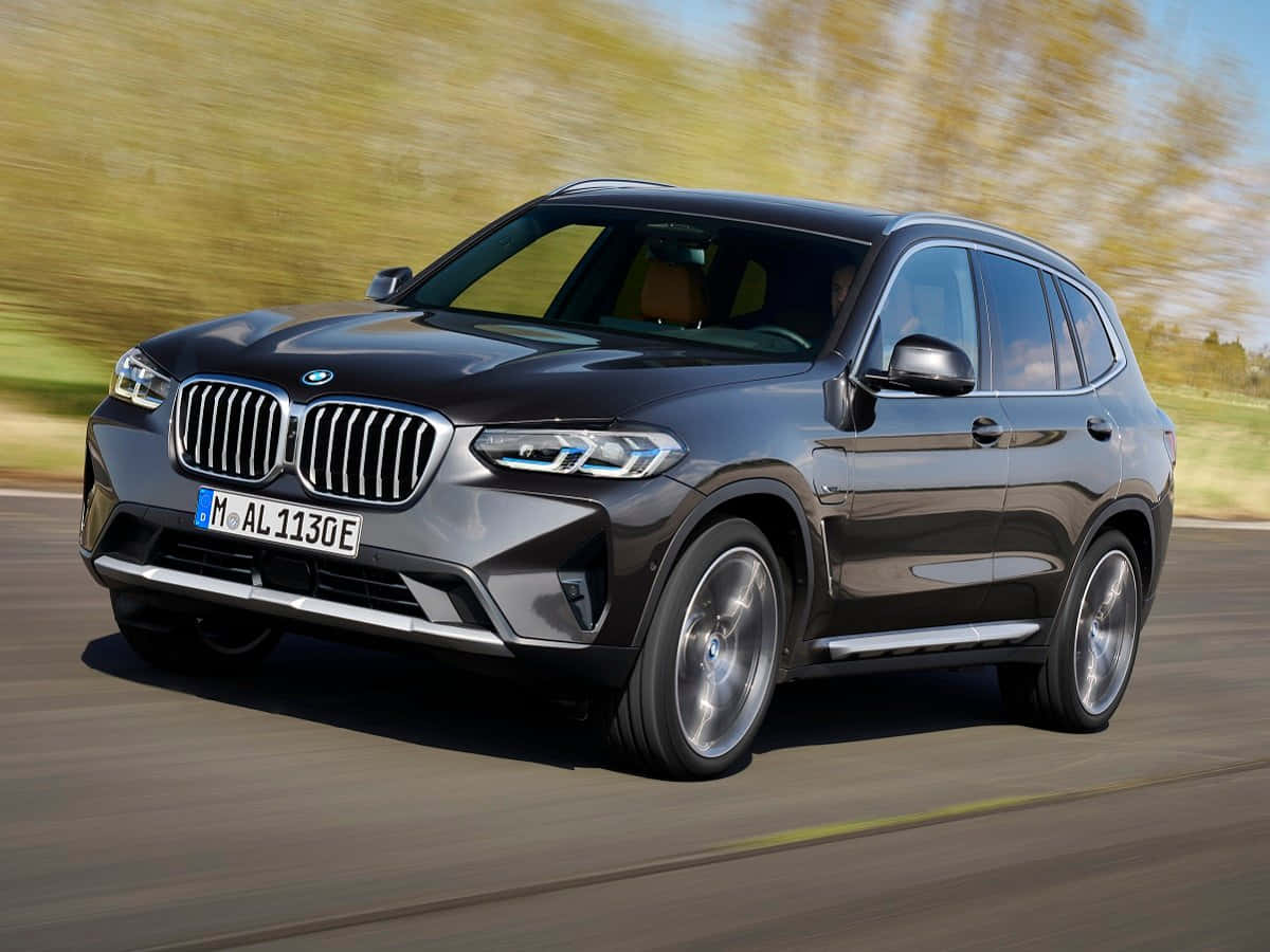 Bmw X5 桌布 壁紙 — 一輛時尚的黑色BMW X3 SUV在道路上疾馳，背景是模糊的金色樹葉。