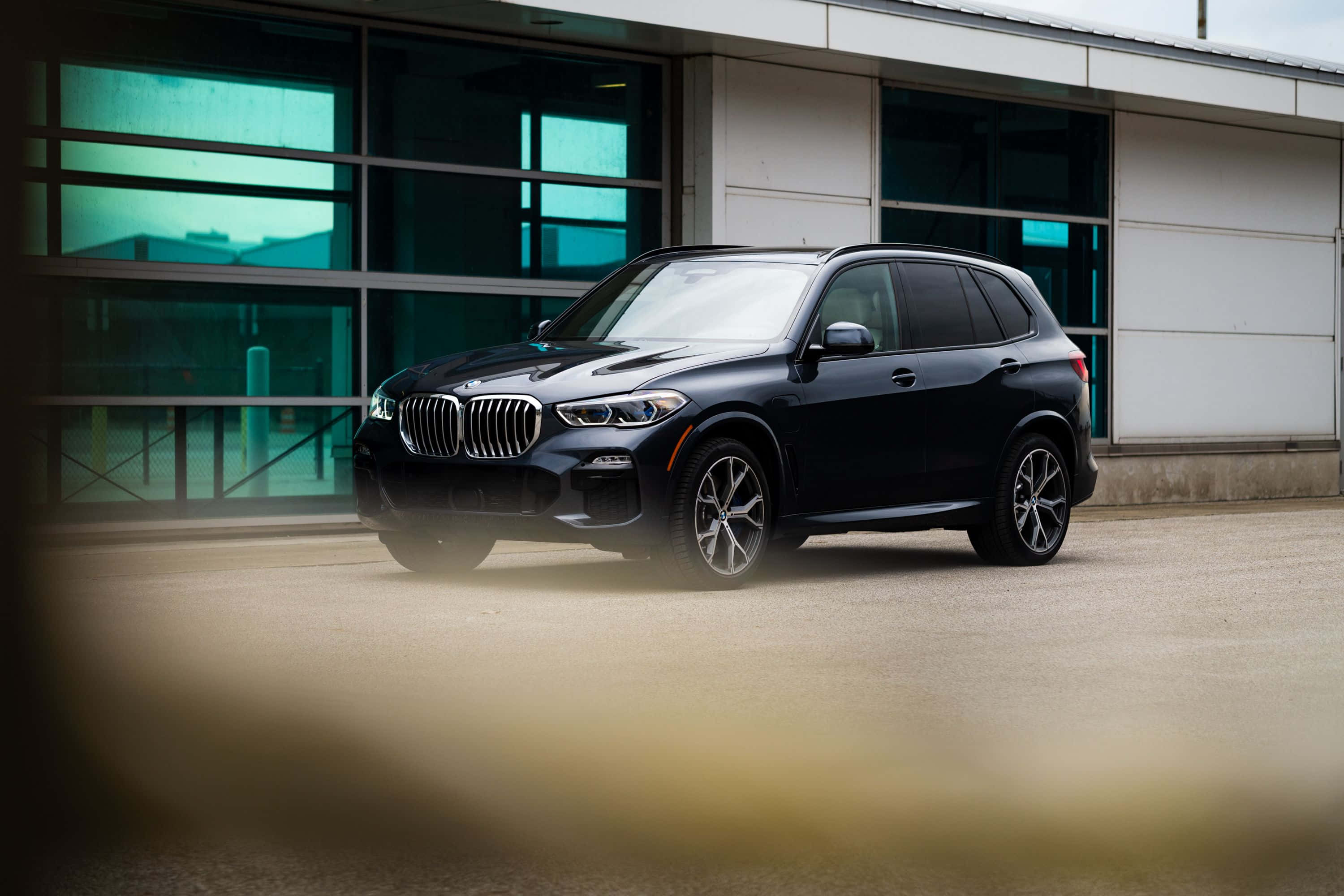 Bmw X5 桌布 壁紙 — 一輛時尚的黑色BMW X5 SUV停在一棟帶有青綠色窗戶的現代建築前。