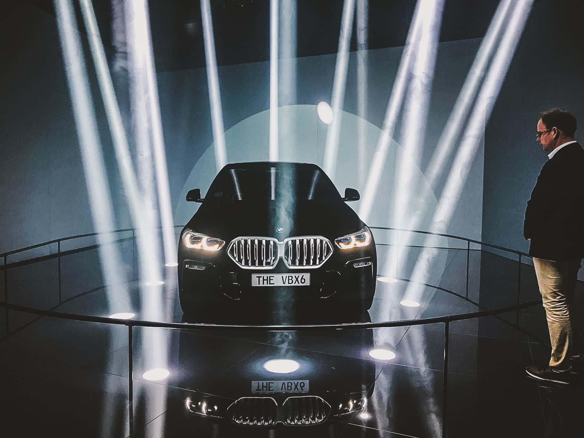 Vantablack 桌布 壁紙 — 一輛時尚的黑色BMW X6在反射舞台上被垂直聚光燈戲劇性地照亮，一名男子從側面觀看。