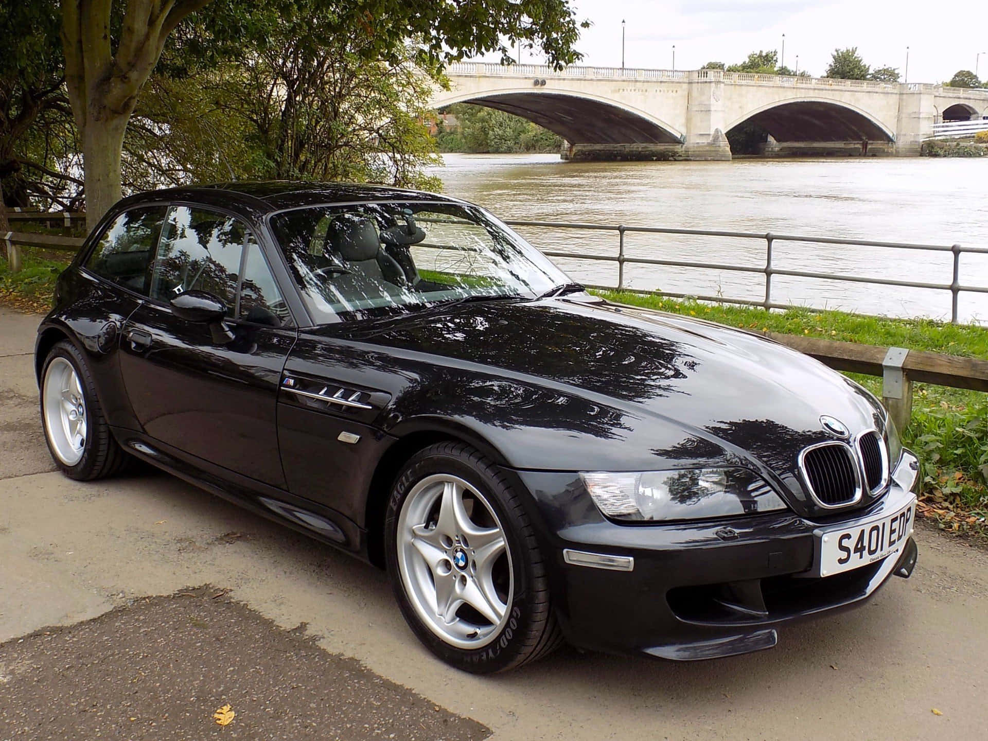 Bmw Z3 桌布 壁紙 — 一輛時尚的黑色BMW Z3開篷跑車停在河邊，背景是一座石橋。