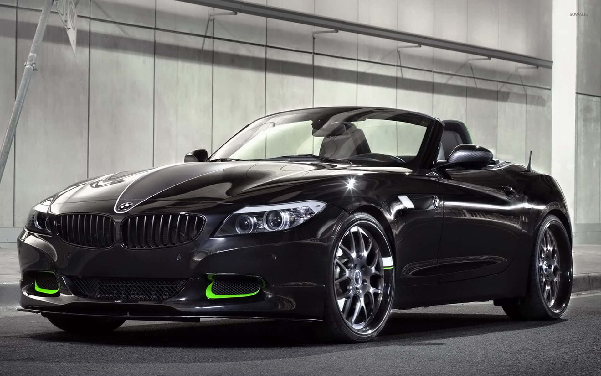Bmw Z4 桌布 壁紙 — 一輛時尚的黑色BMW Z4開篷車帶有螢光綠色點綴，在現代混凝土車庫的攝影棚燈光下閃閃發光。