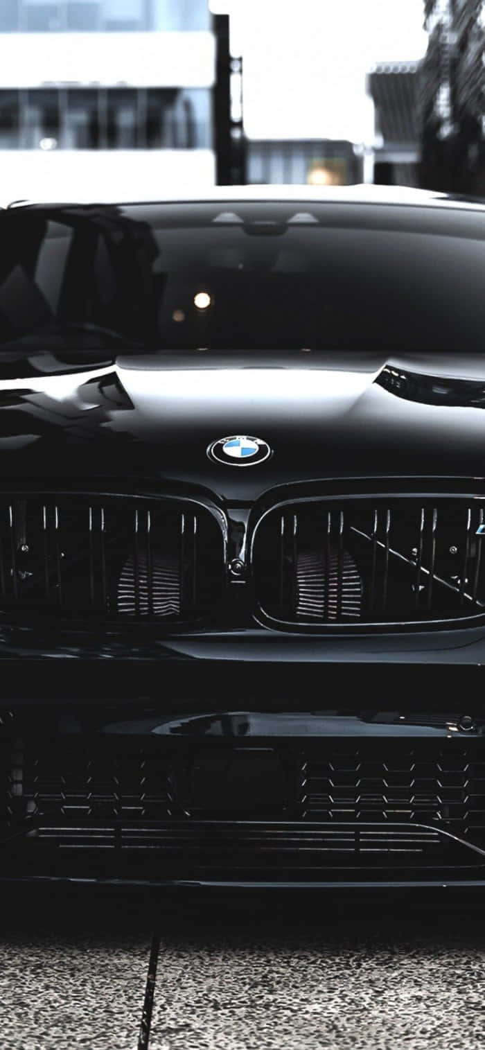 BMW M iPhone 壁紙 — 一輛時尚的黑色BMW跑車在都市日光下閃耀，具有光澤表面和銳利的格柵細節。