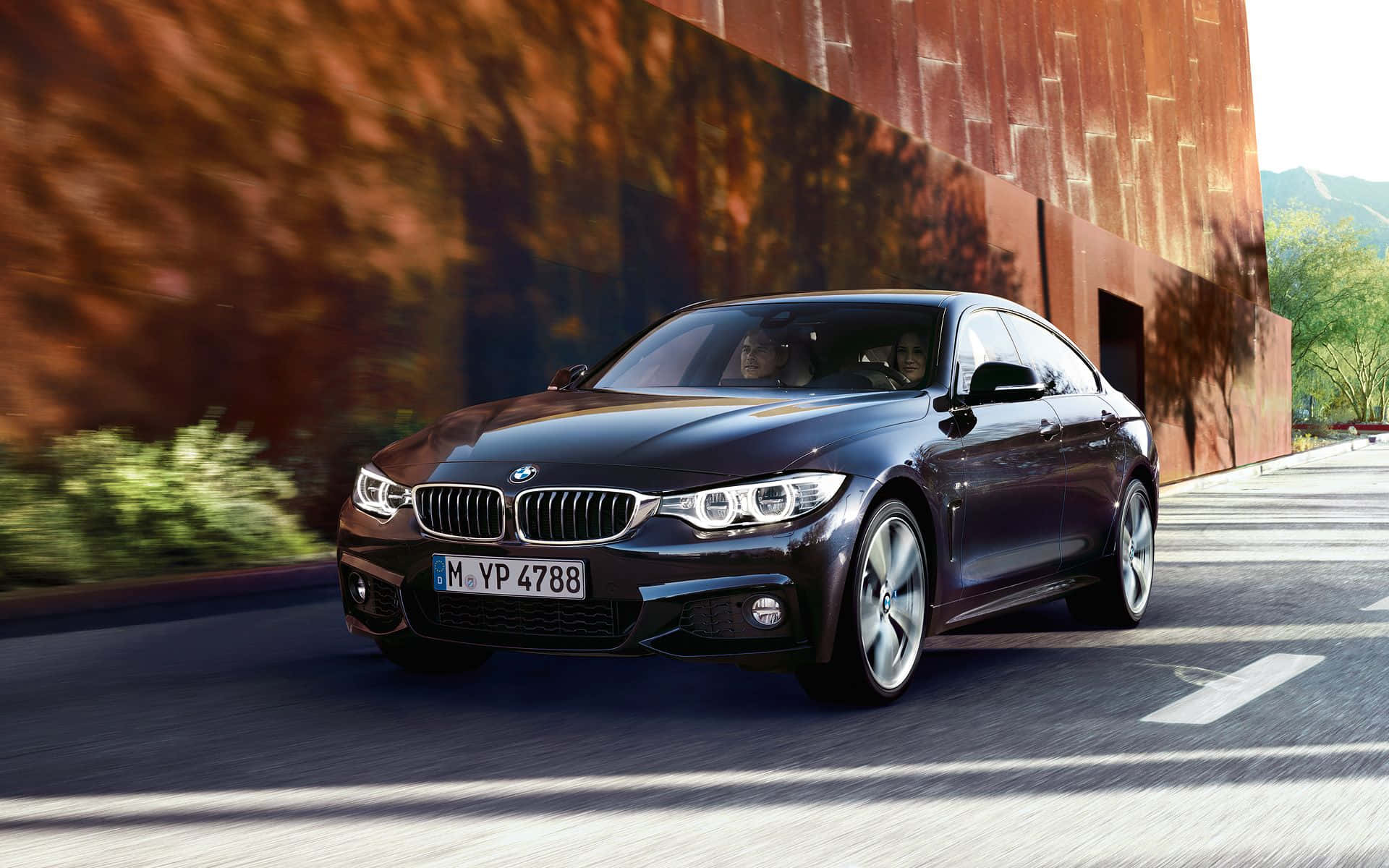 Bmw 4 Series 桌布 壁紙 — 一輛時尚的黑色BMW雙門跑車在陽光普照的道路上，沿著鏽色牆壁疾馳，帶有動態模糊效果。