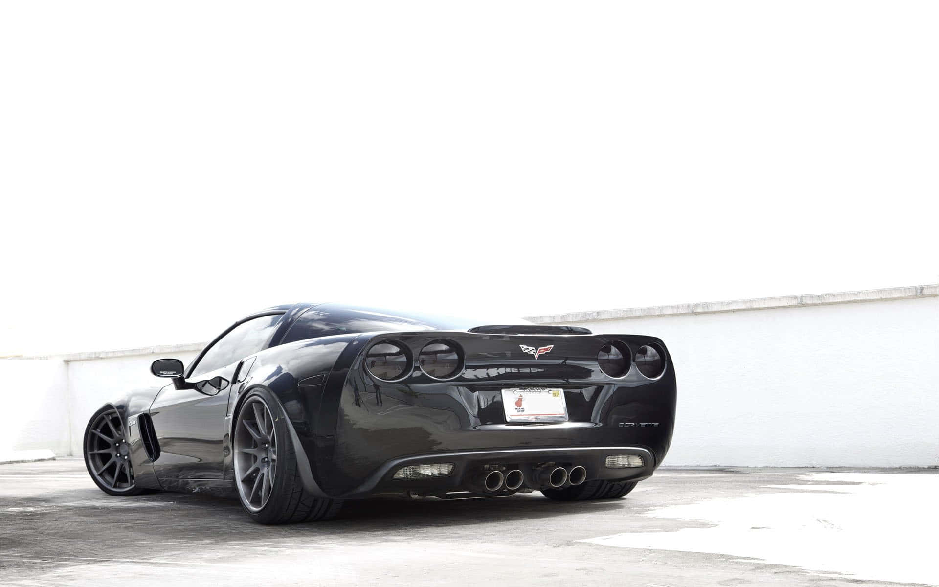 Chevrolet Corvette Z06 桌布 壁紙 — 一輛時尚的黑色Corvette跑車在明亮的日光下停放在簡約的白色牆壁前。